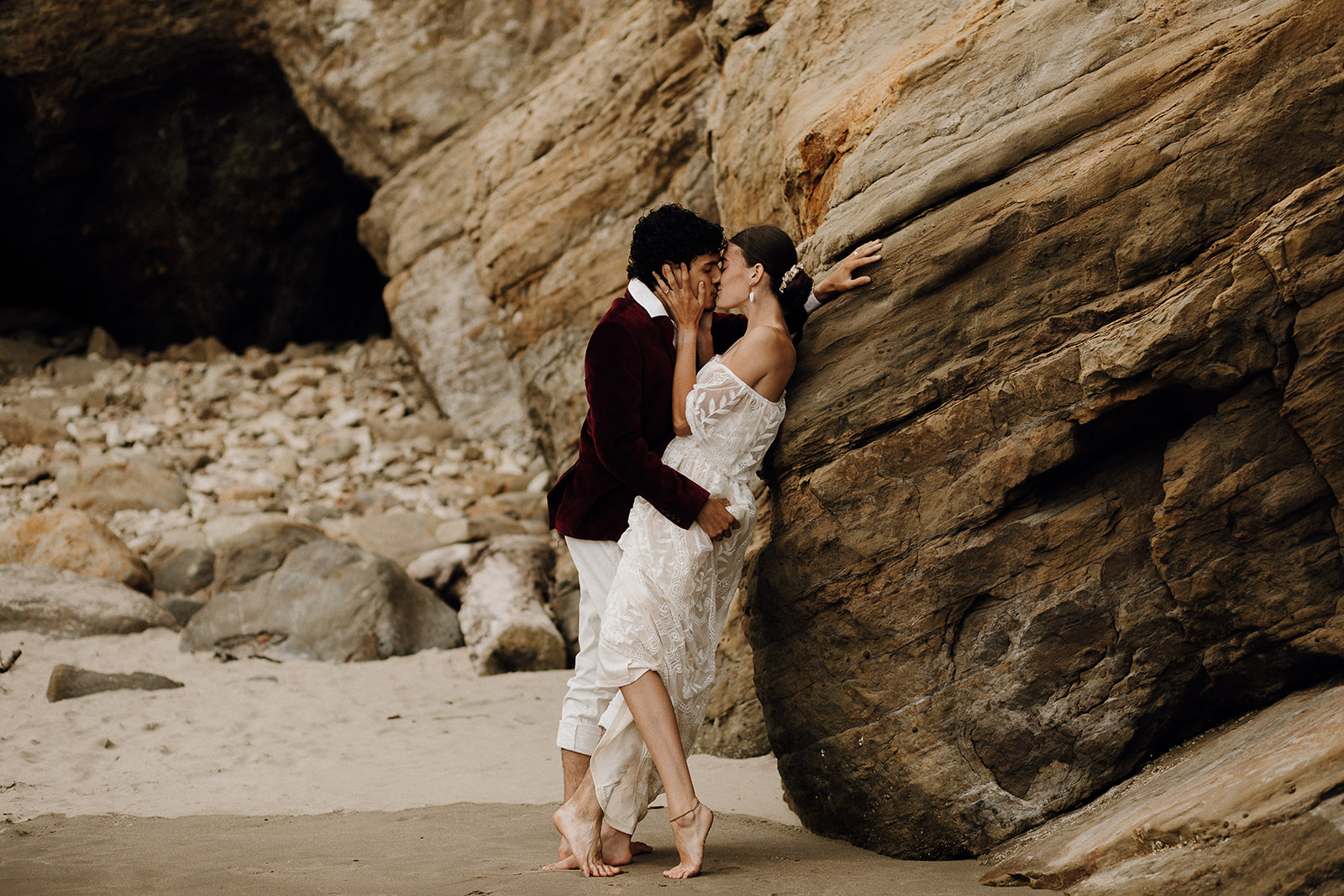 Bride and groom kissing up against a rock on the beach at Devil's Punchbowl