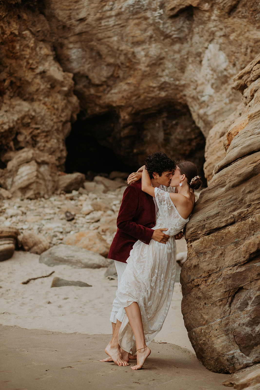 Bride and groom kissing up against a rock on the beach at Devil's Punchbowl