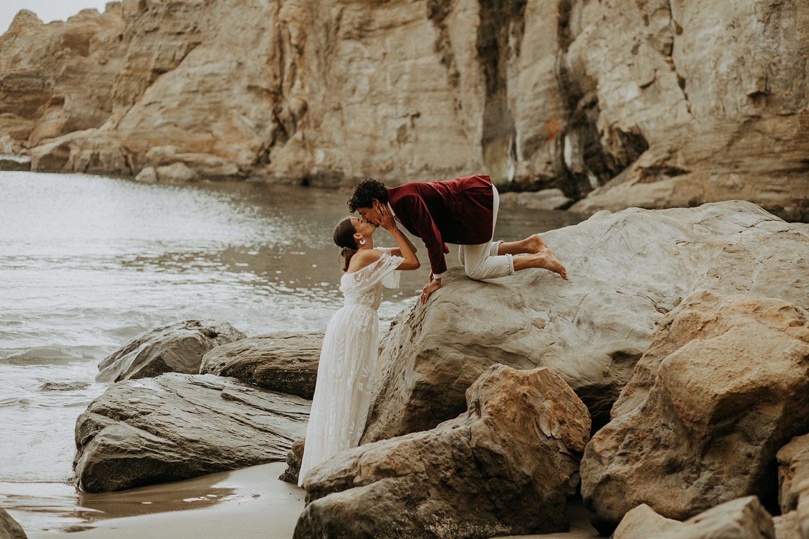 Groom kneeling on a rock and leaning down to kiss bride at Devil's Punchbowl