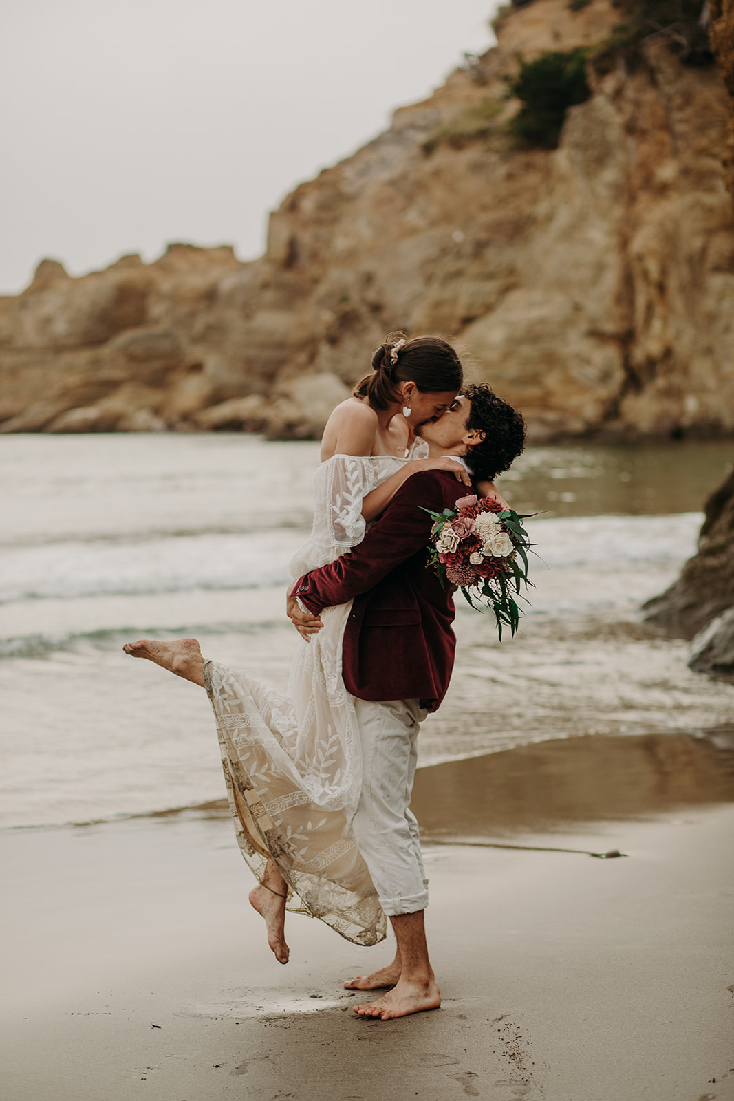 Groom picking up bride and kissing on the beach at Devil's Punchbowl