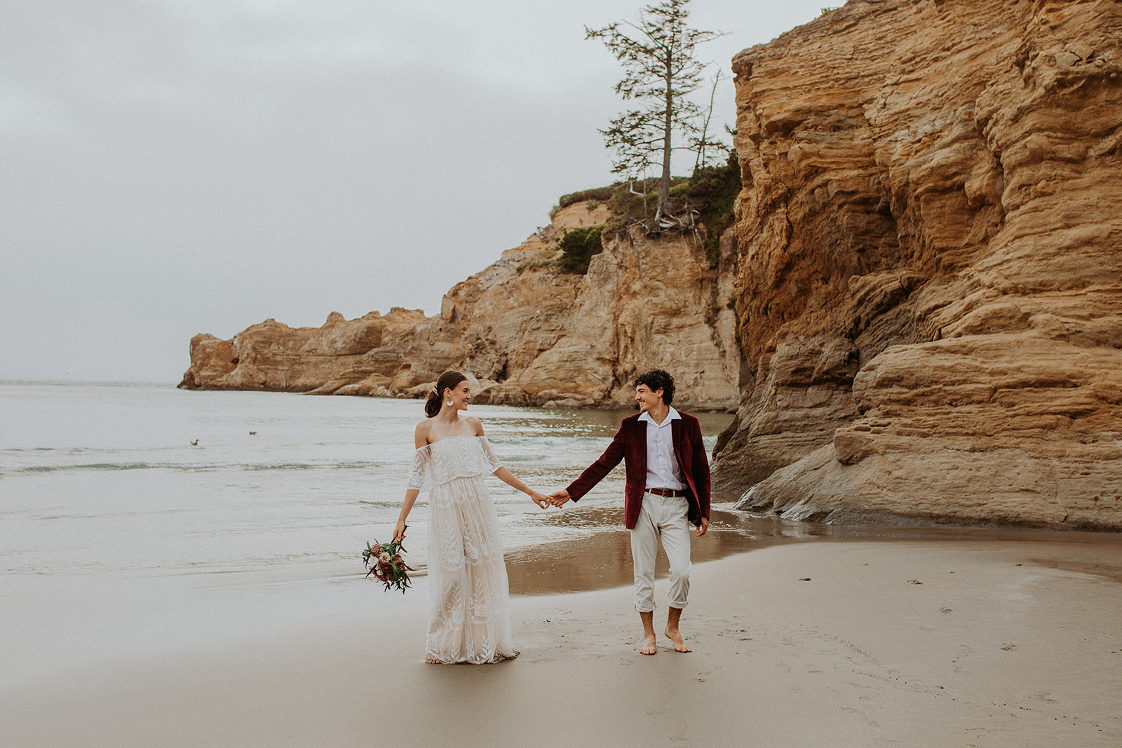 Bride and groom holding hands walking down the beach for their Oregon Coast elopement