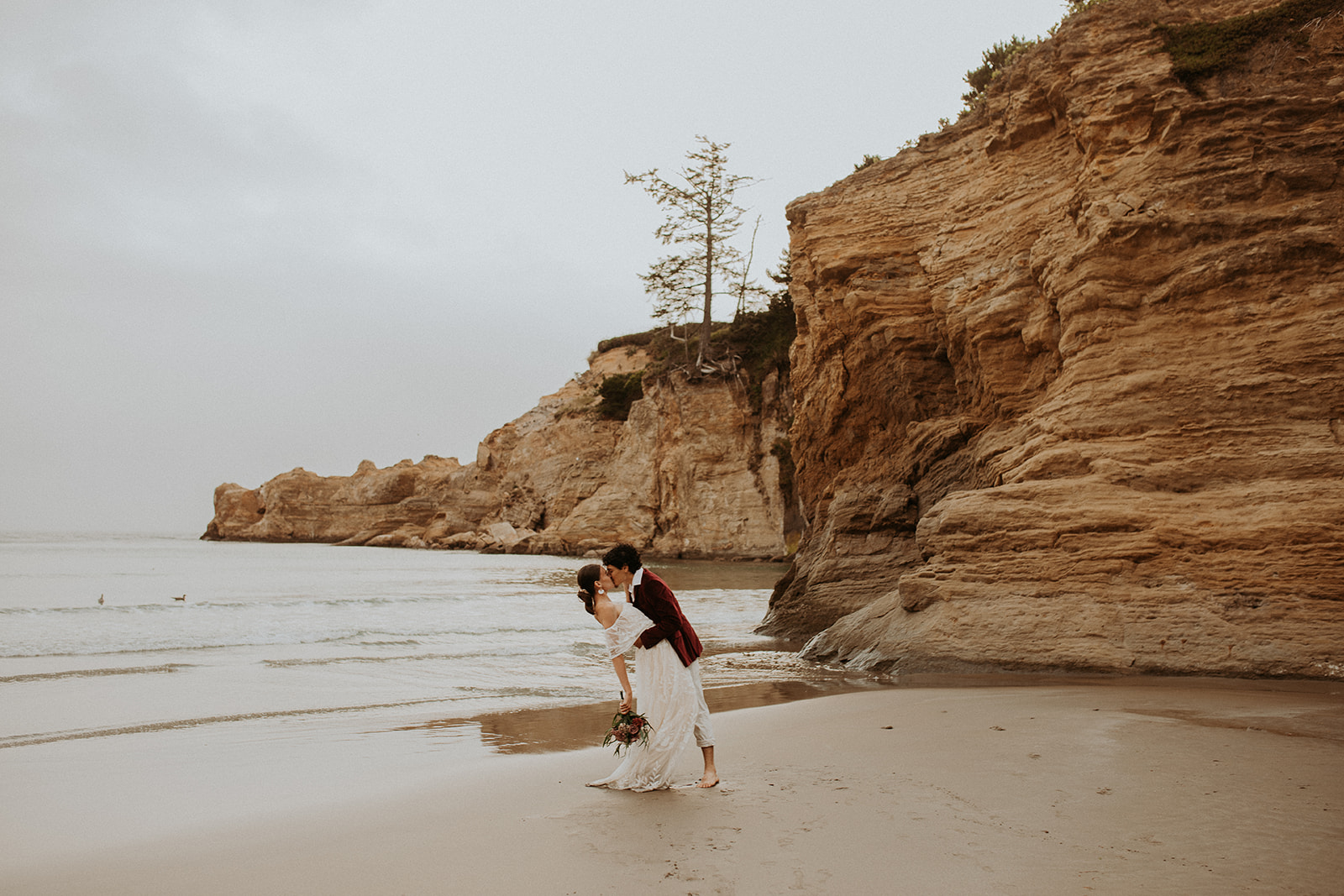 Groom dipping bride back and kissing her on the beach for their Oregon Coast elopement