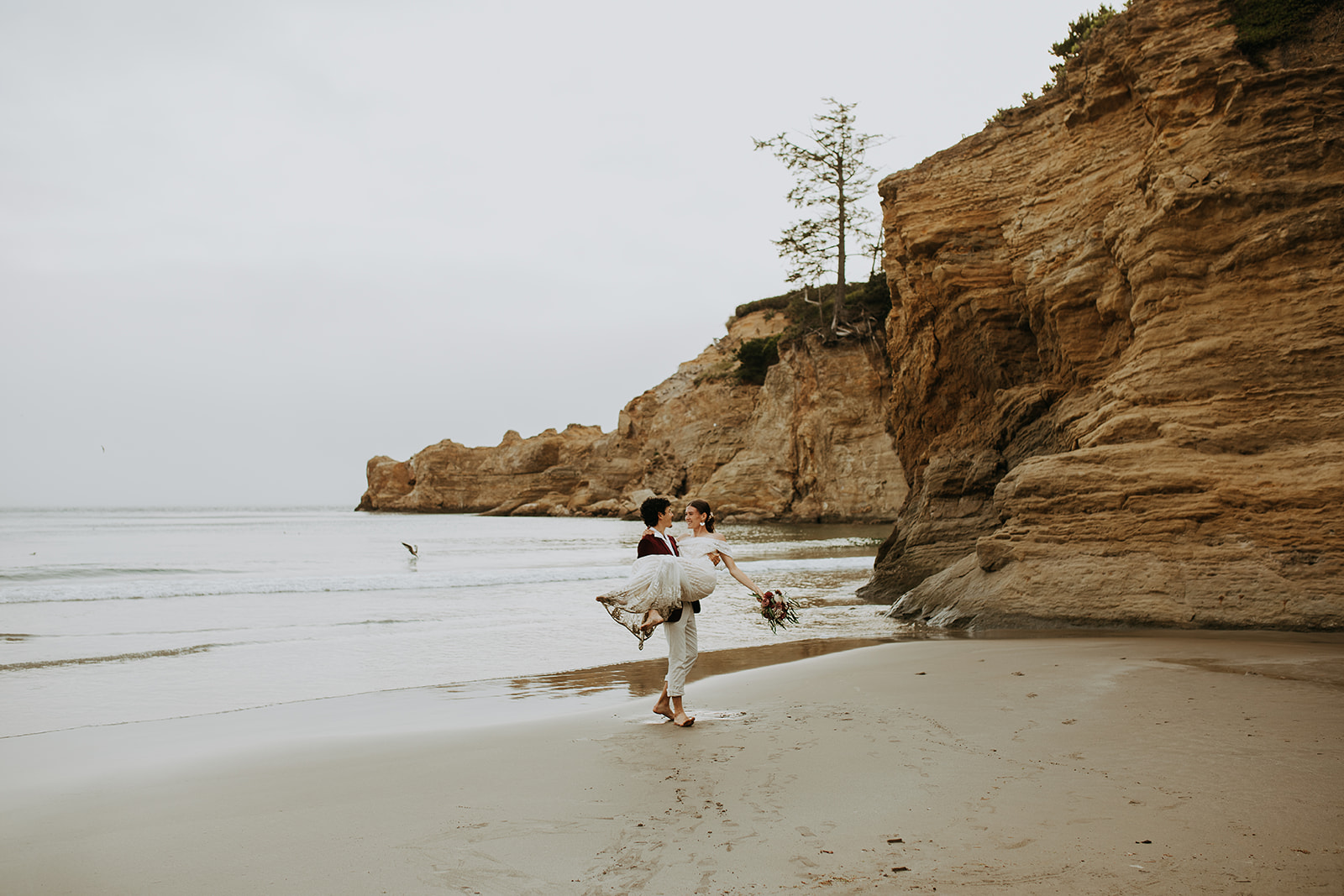 Groom carrying bride and twirling her on the beach for their Oregon Coast elopement