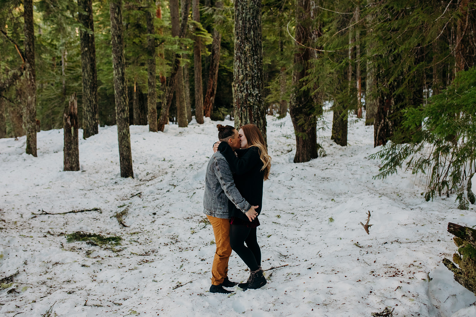 Two women kissing in the snowy forest for engagement photos