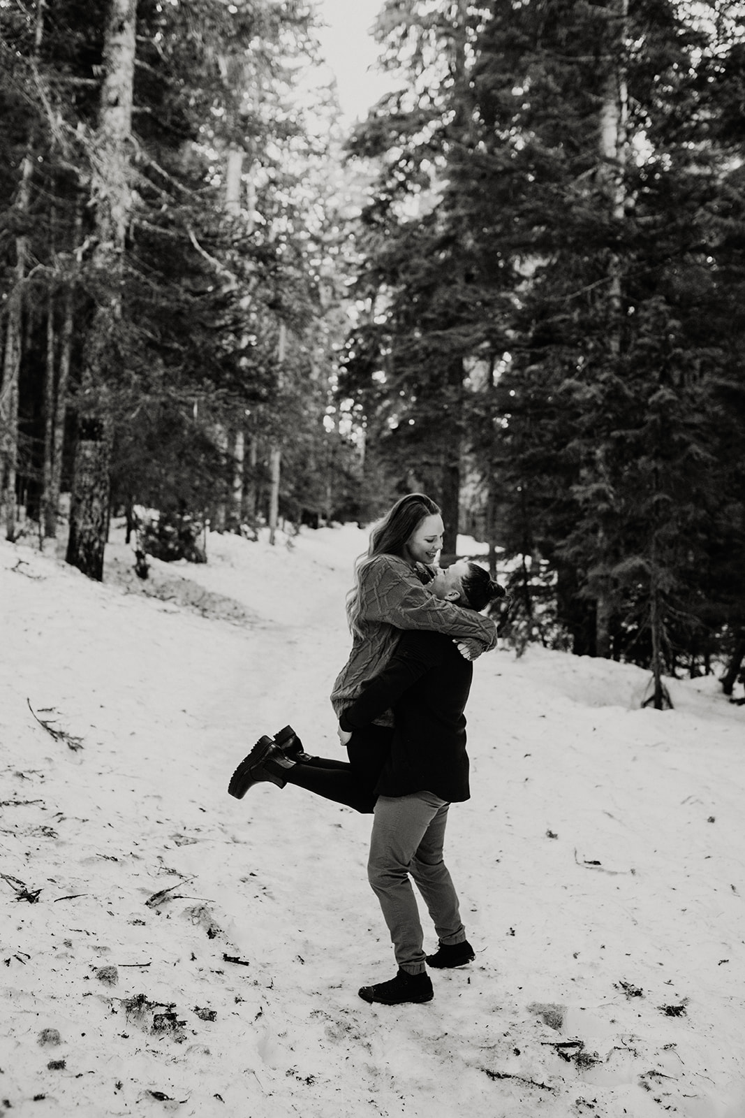 Woman picking her partner up during snowy engagement photos