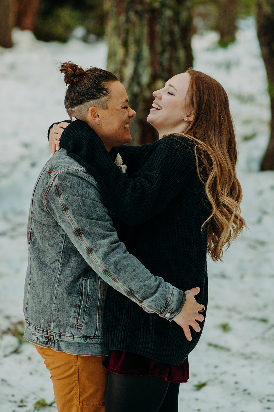 Two women hugging and laughing in the snow during snowy engagement photos