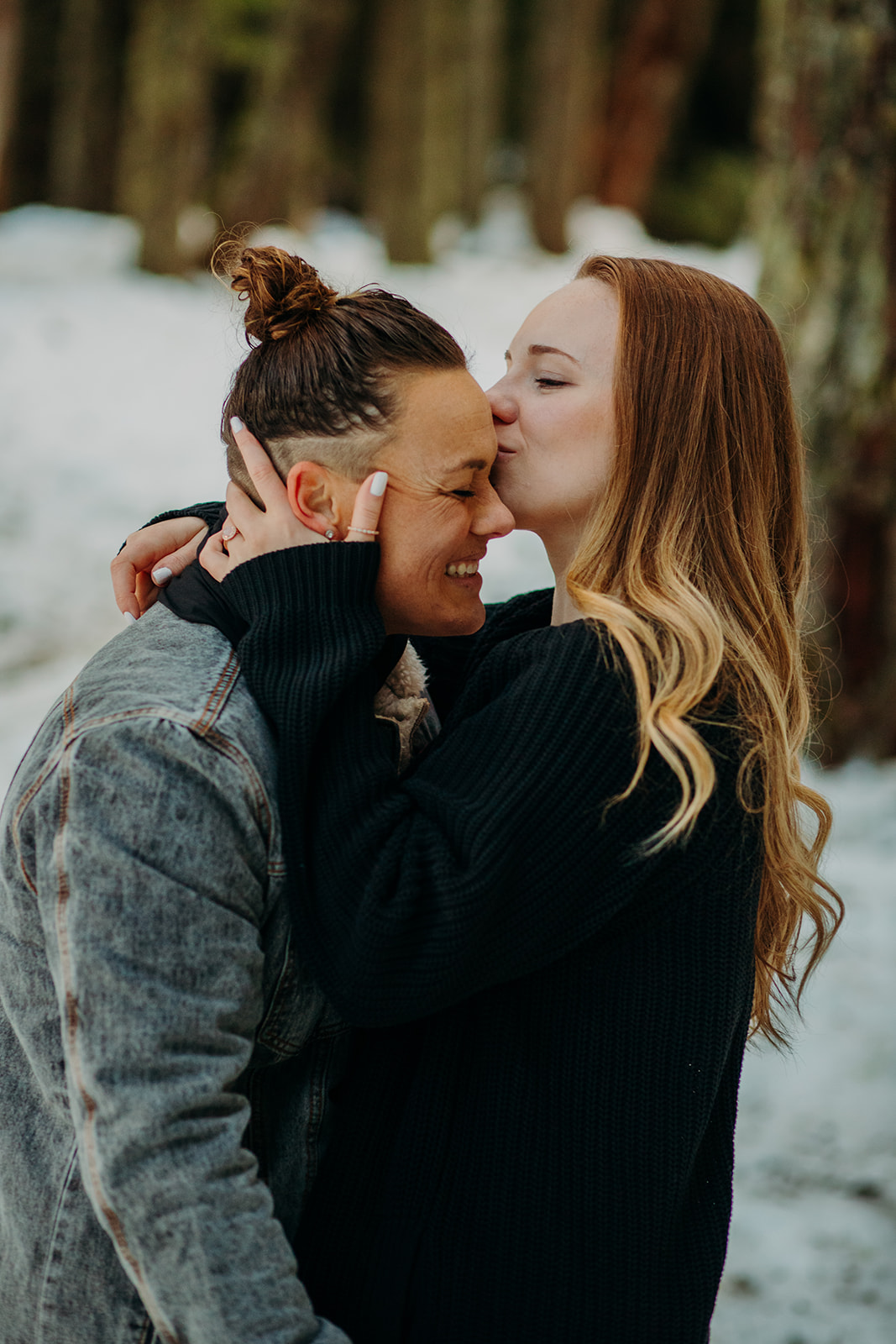 Woman kissing her partner on the forehead during snowy engagement session