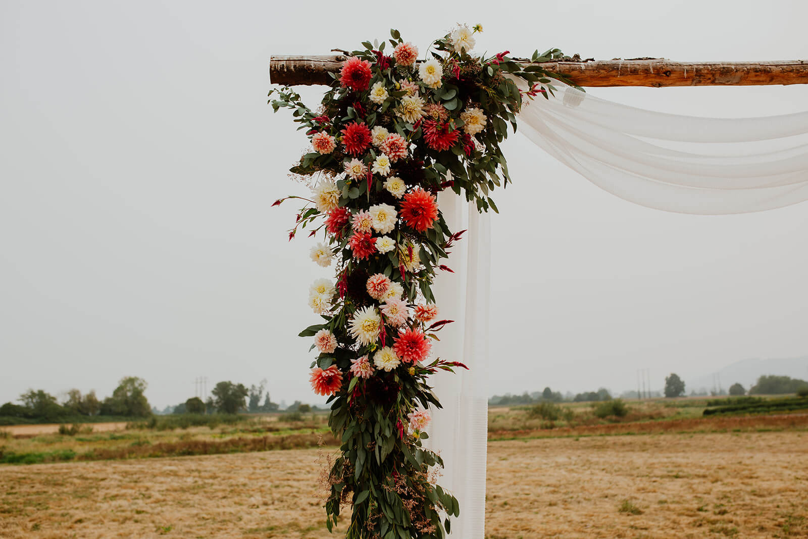 Peach, pink, and white floral arrangement handing on wood wedding arch
