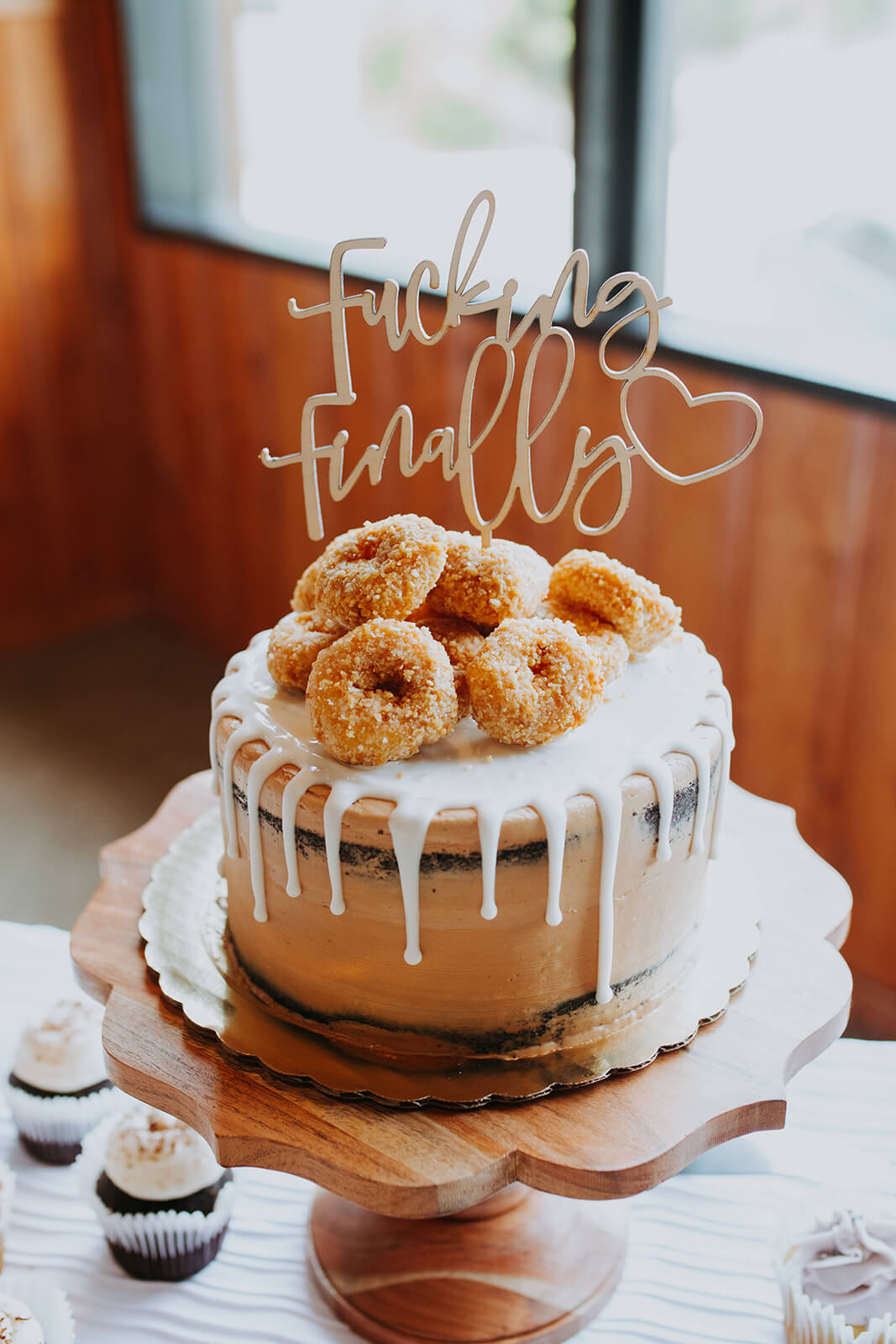 White wedding cake topped with doughnuts and "fucking finally" sign