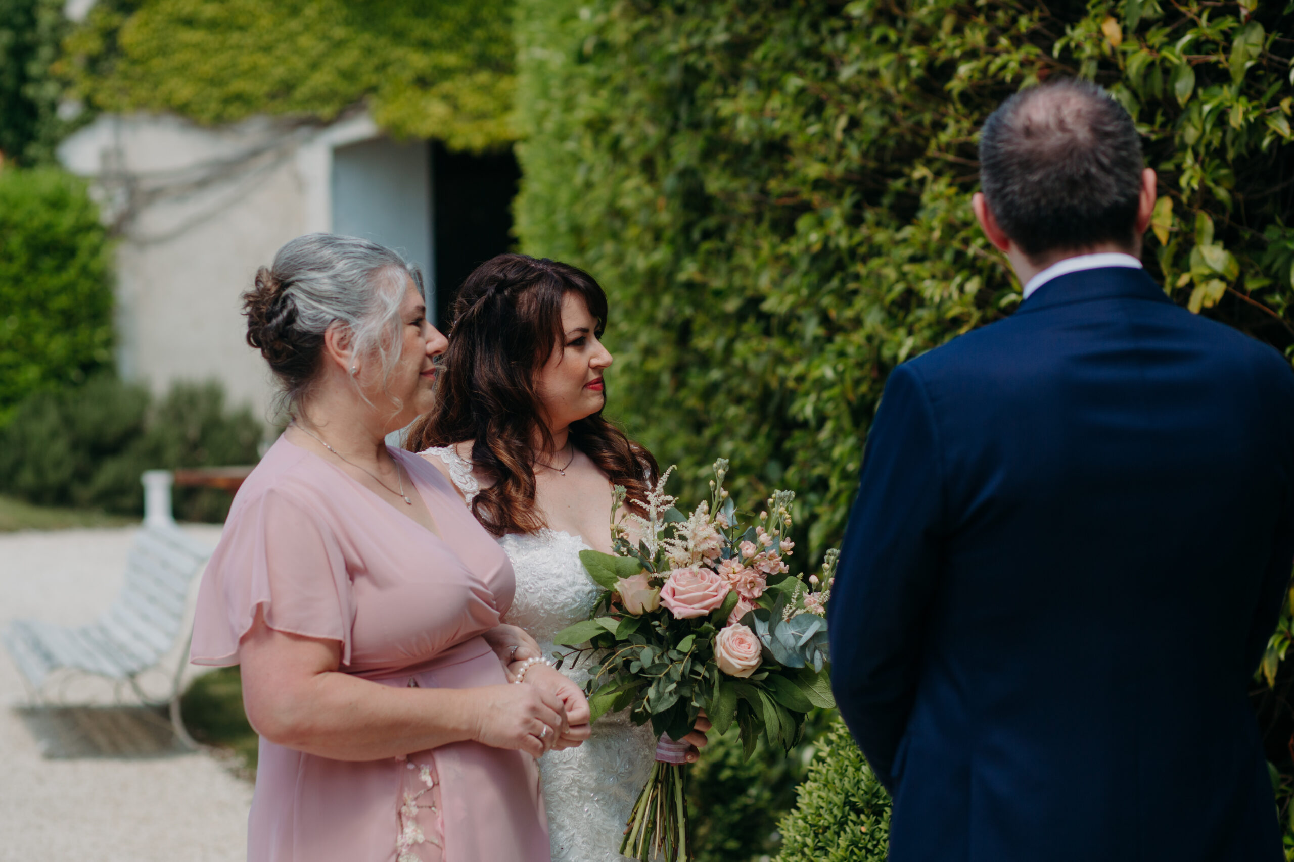 A mother in pink stands next to her daugher and future son in law at a wedding ceremony. 