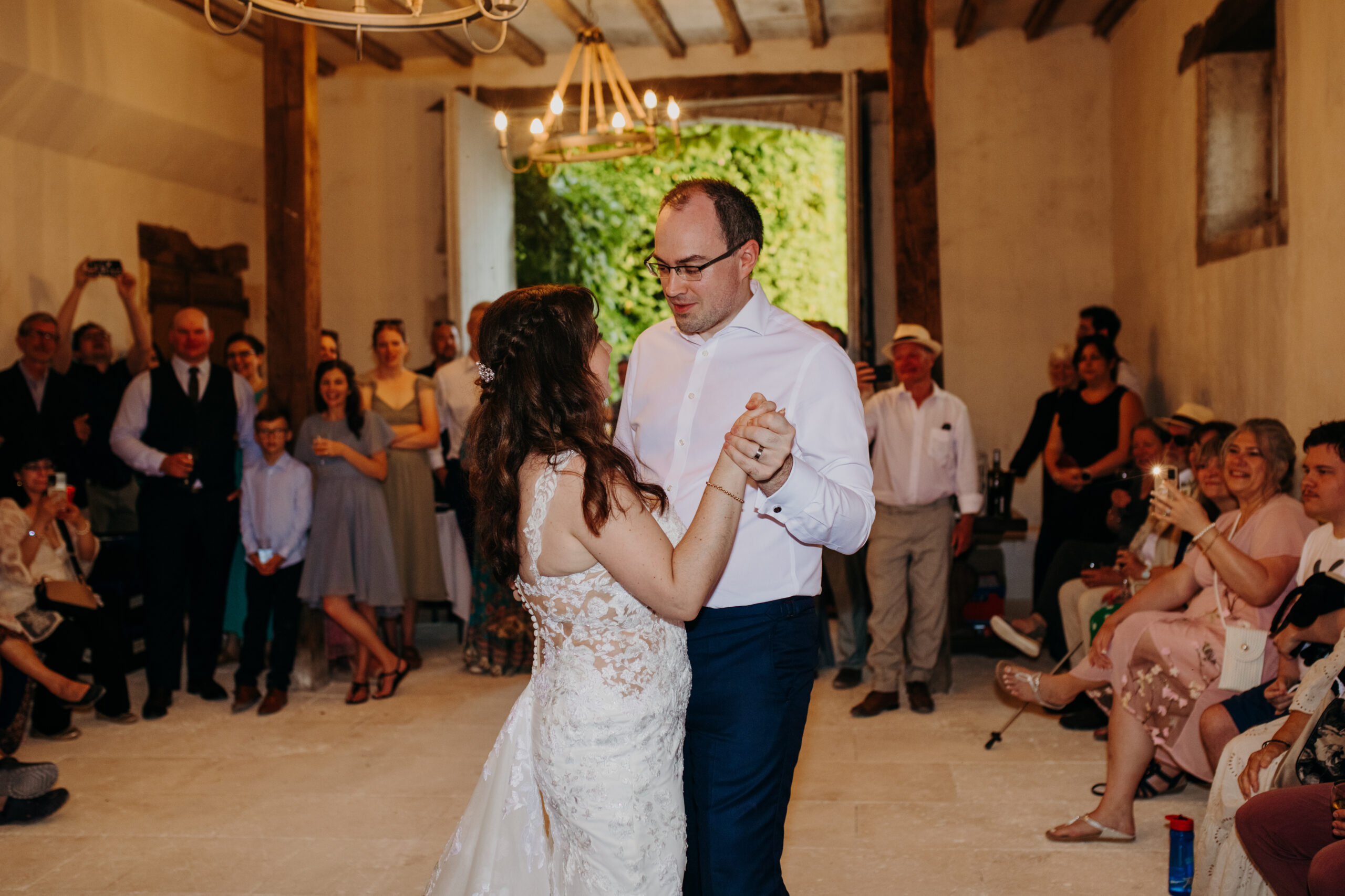 man and woman stand in a room full of their friends as they enjoy their first dance as a married couple