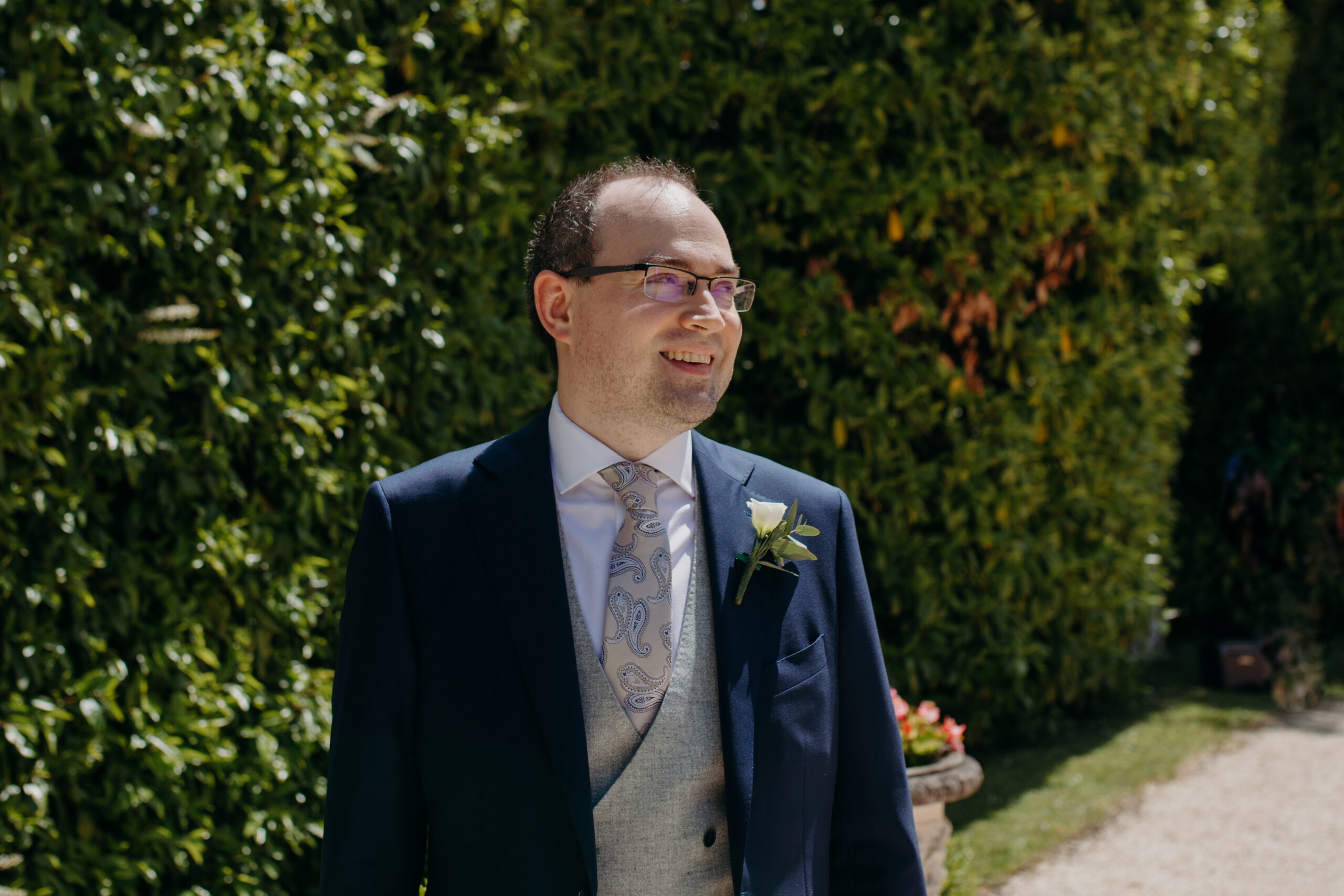 A groom stands outside smiling. 