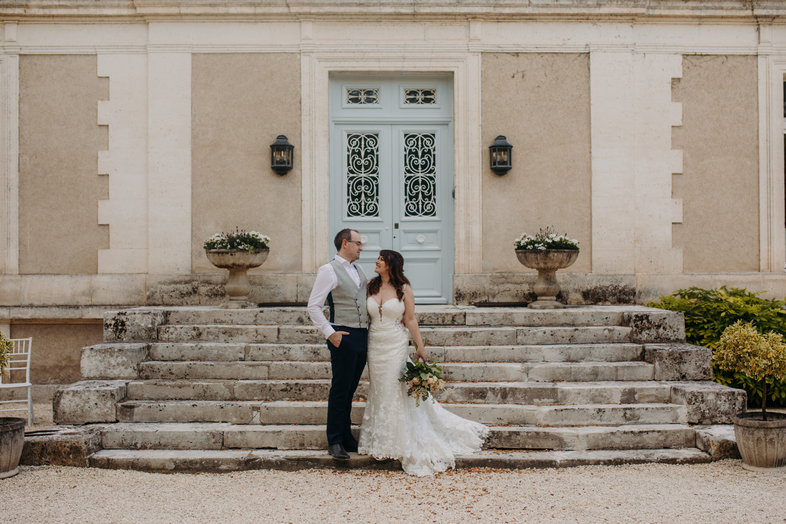 bride and groom stand on steps of chateau smiling at each other