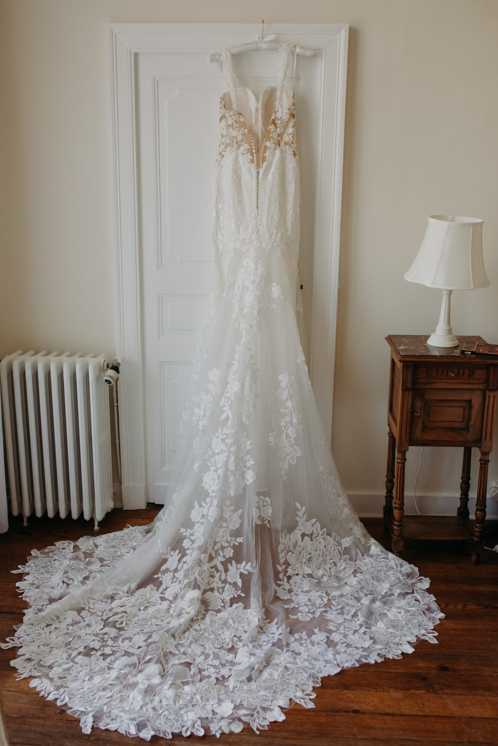 a bride's wedding dress hangs from a white door with a long lacy train