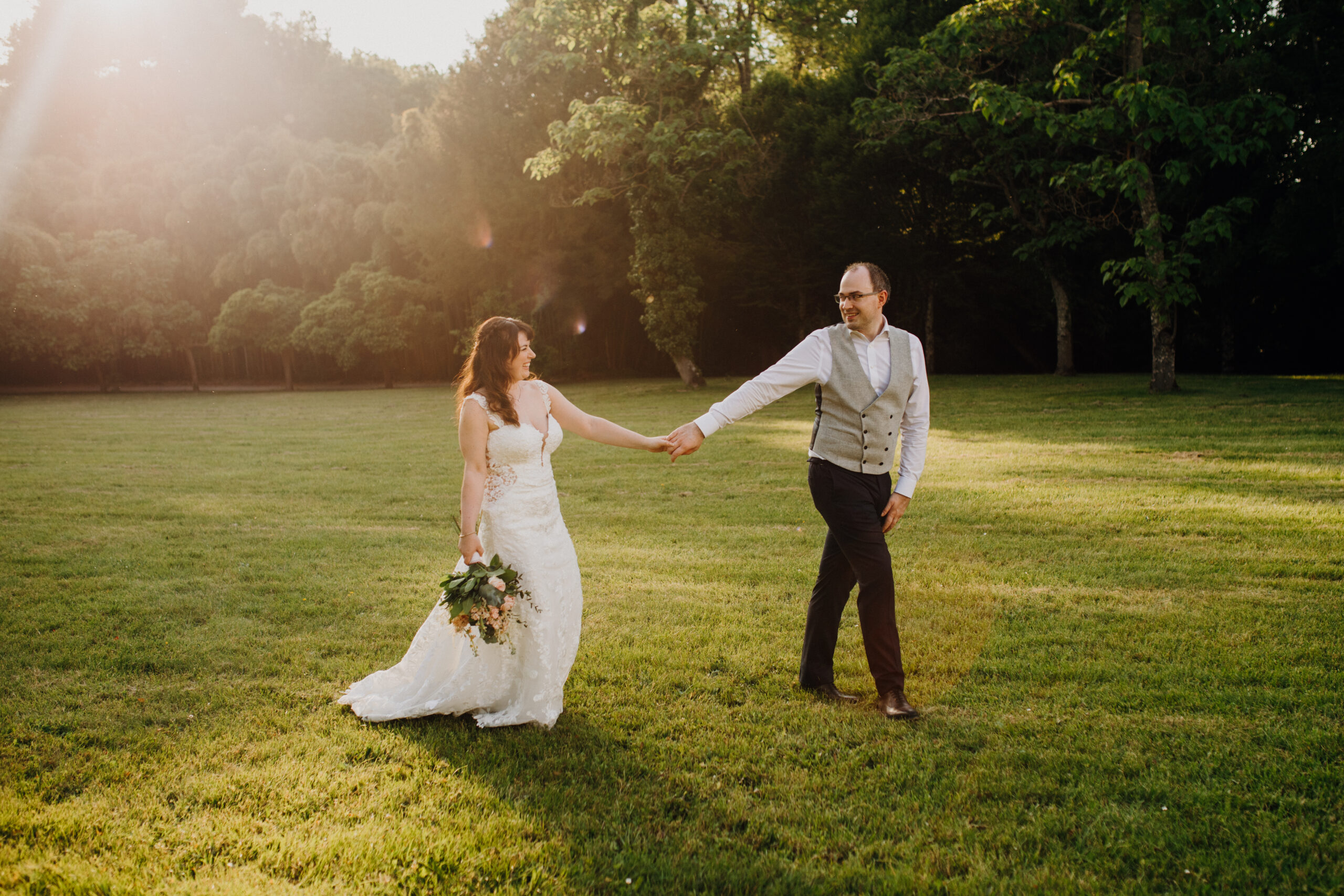 bride and groom stroll through a grassy field hand in hand smiling at each other. 
