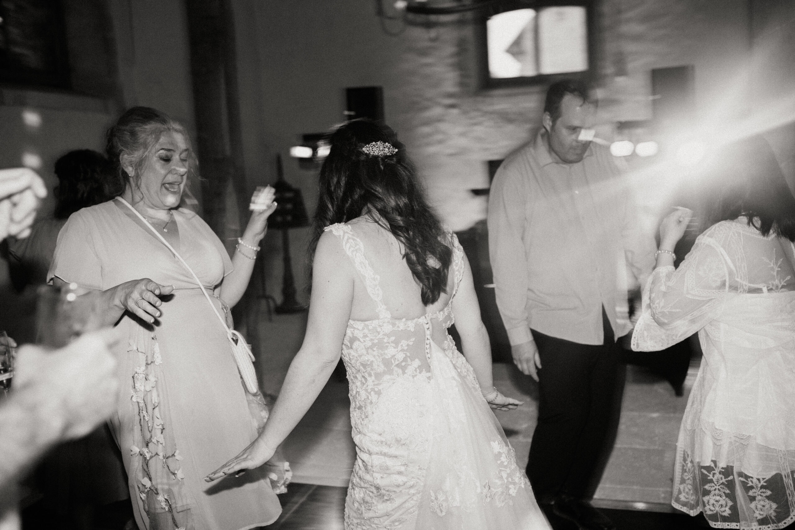 woman and bride dance excitedly in this black and white photo with guests dancing nearby 
