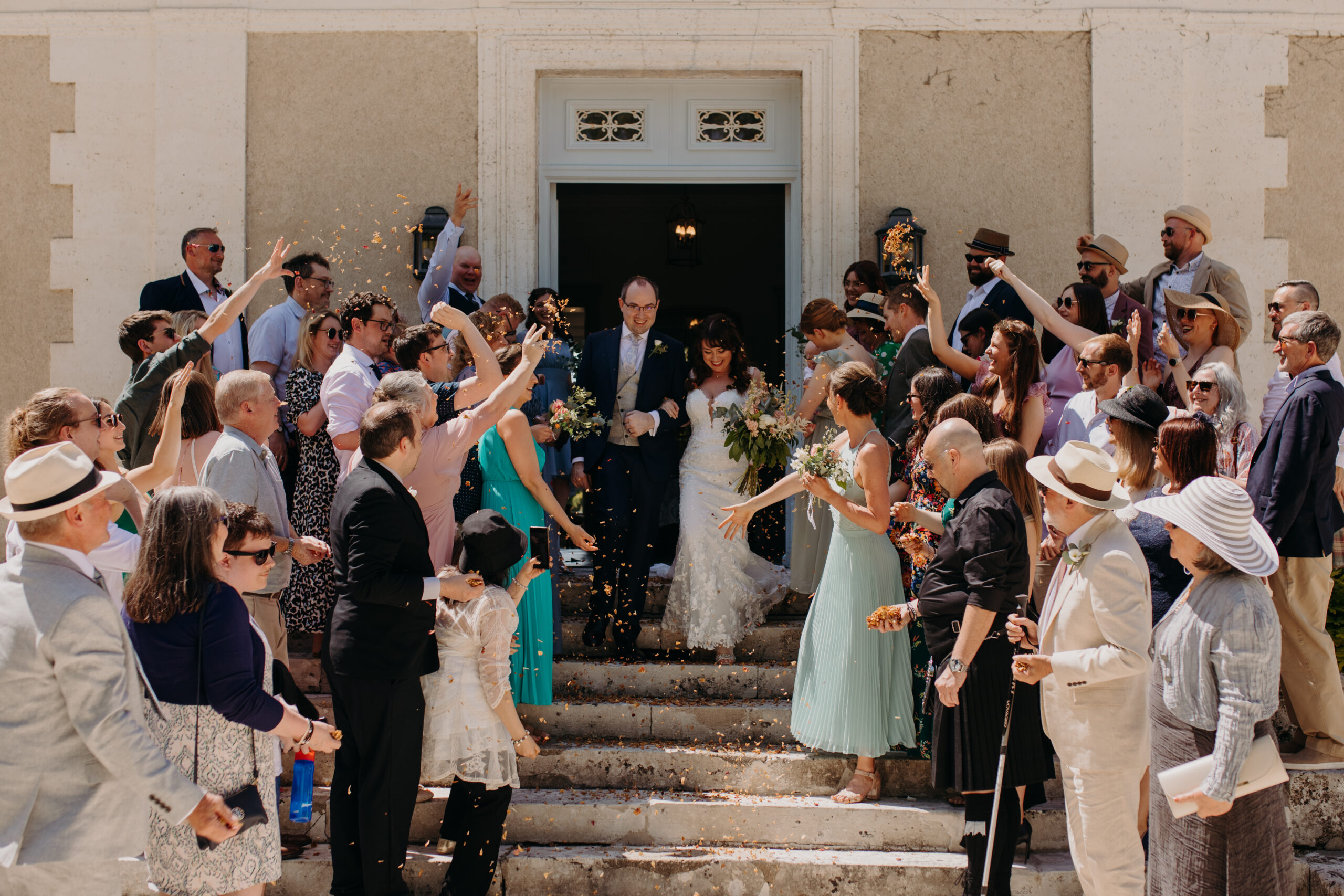 people gather on steps of chateau and throw rose petals towards bride and groom
