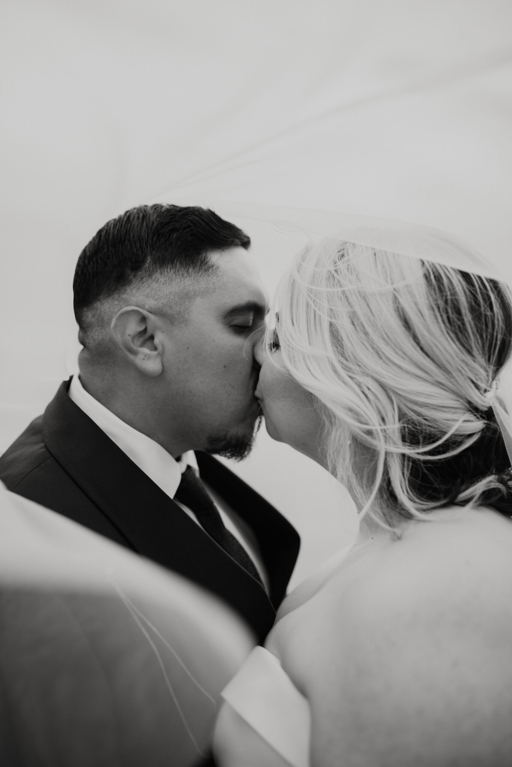 black and white photo of man and woman kissing with a white veil swirling around them