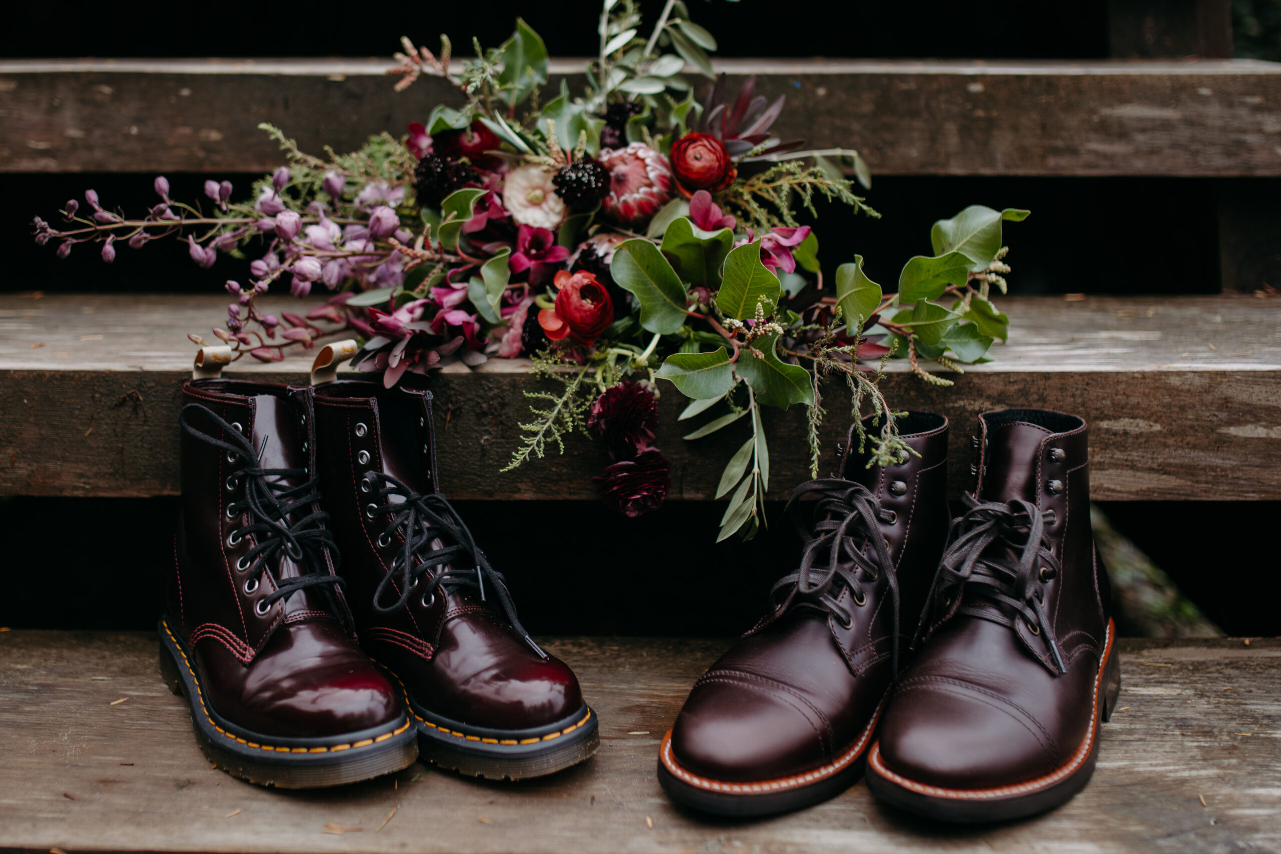 two pairs of doc marten boots sit on stairs with bouquet of flowers on step behind them