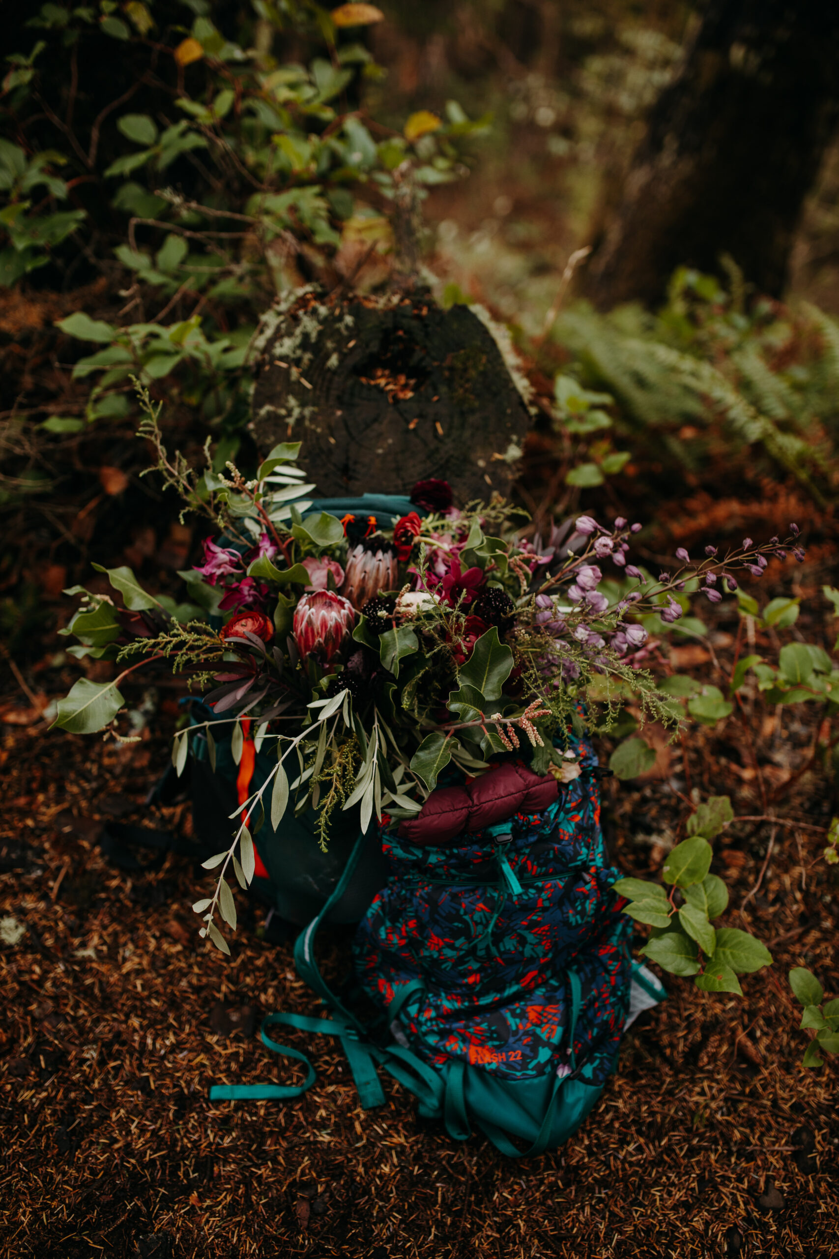 floral bouquet bursts out of hiking backpack sitting on forest floor