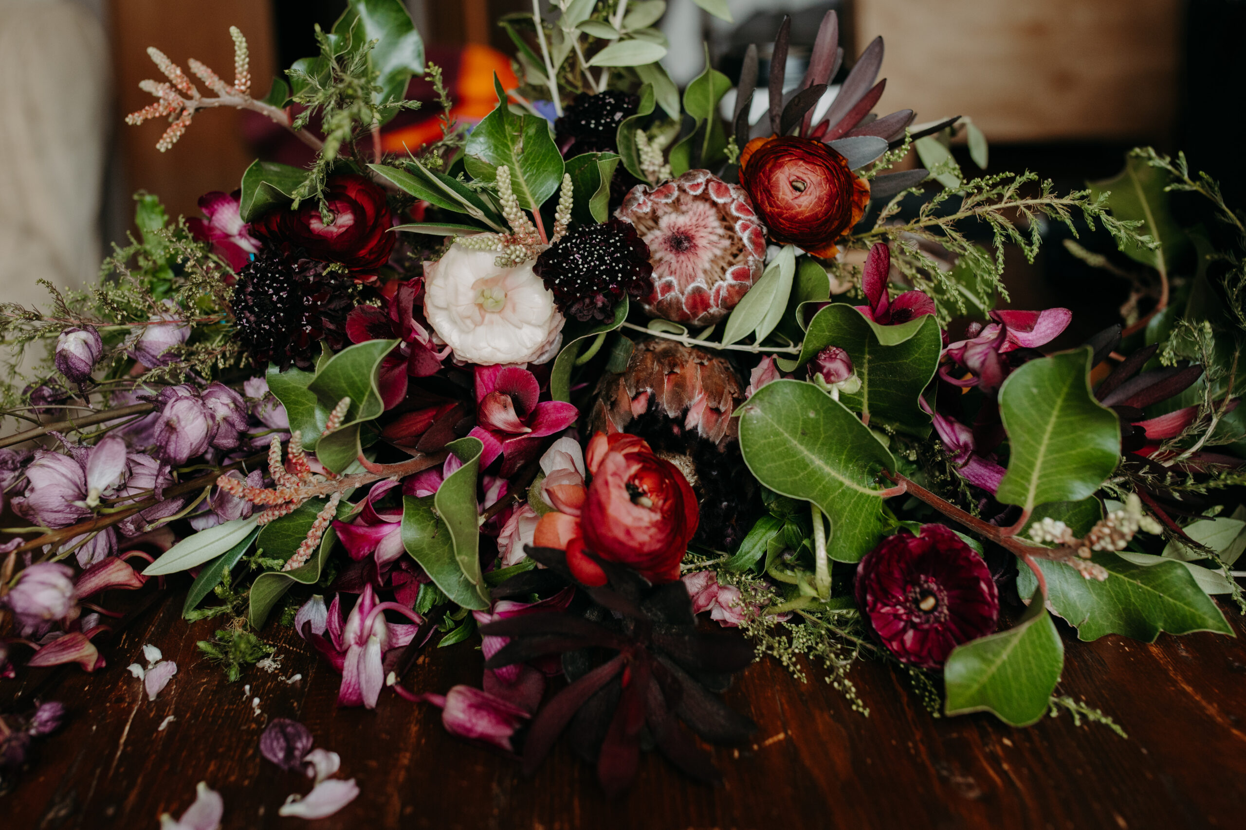floral bouquet lies on a wooden table with green leaves, red, purple, and white flowers 