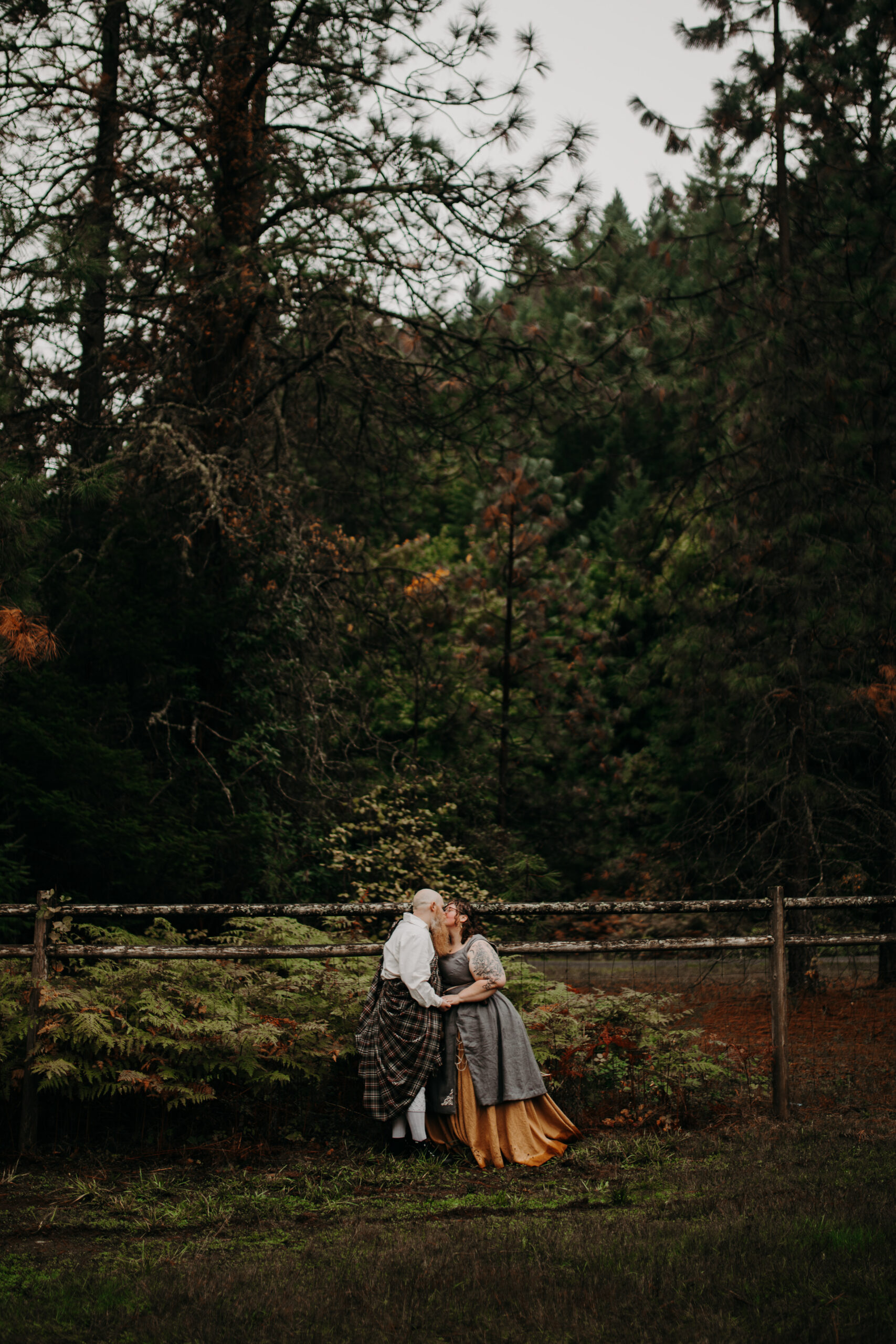 man and woman kiss in medford oregon with forest behind them