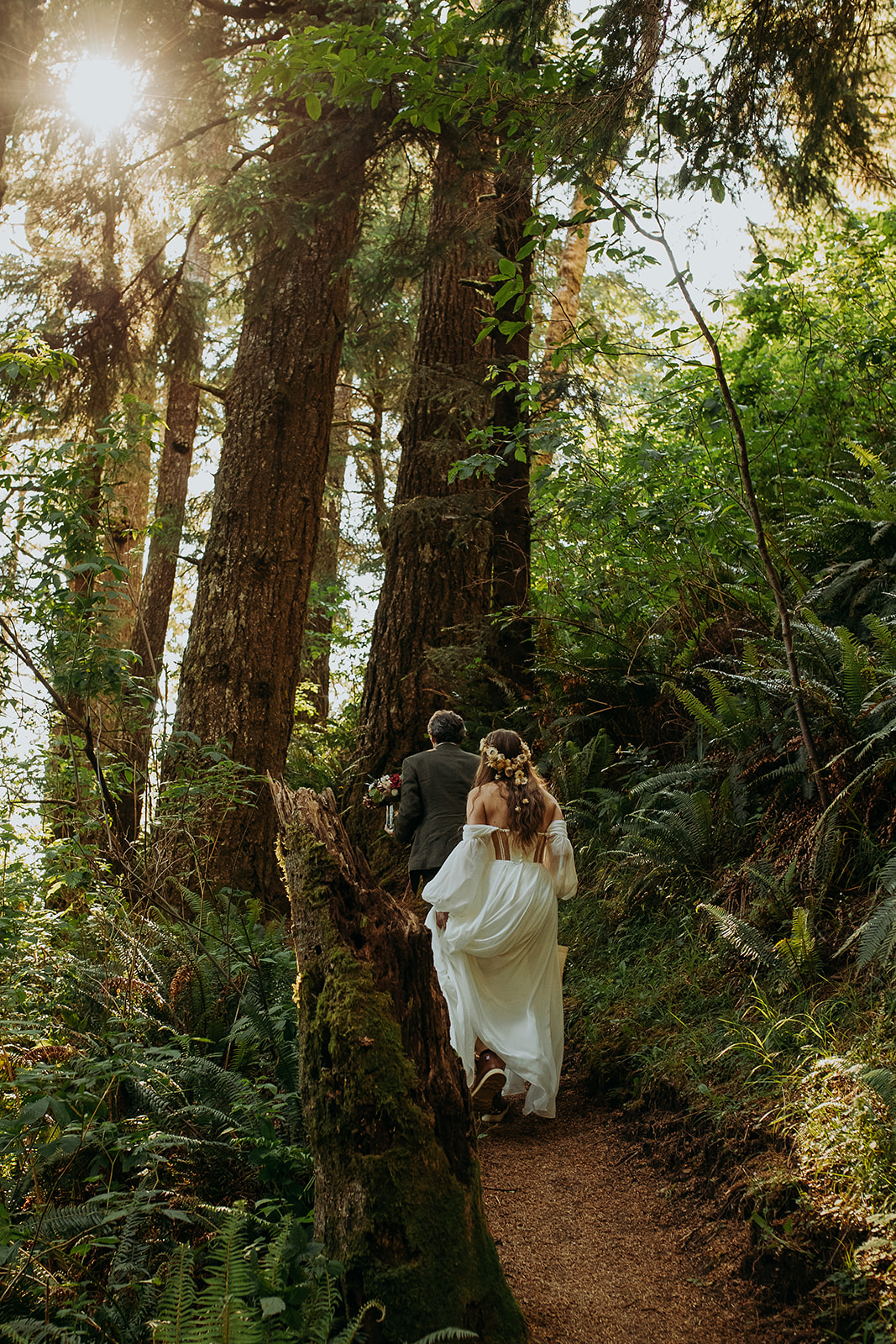 a couple in elopement attire walk the Samuel H. Boardman scenic corridor trail through the forest on a narrow path.