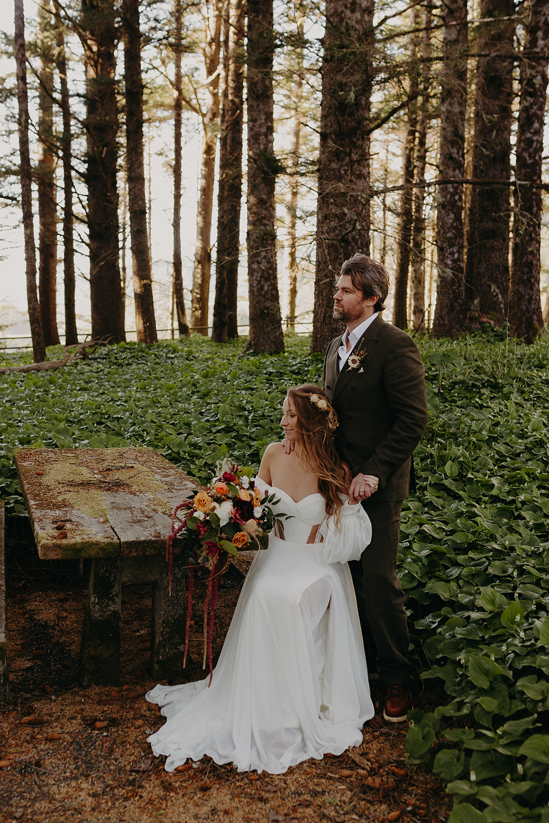 A couple sit near a picnic table amidst a forested trail for this Brookings, Oregon elopement.