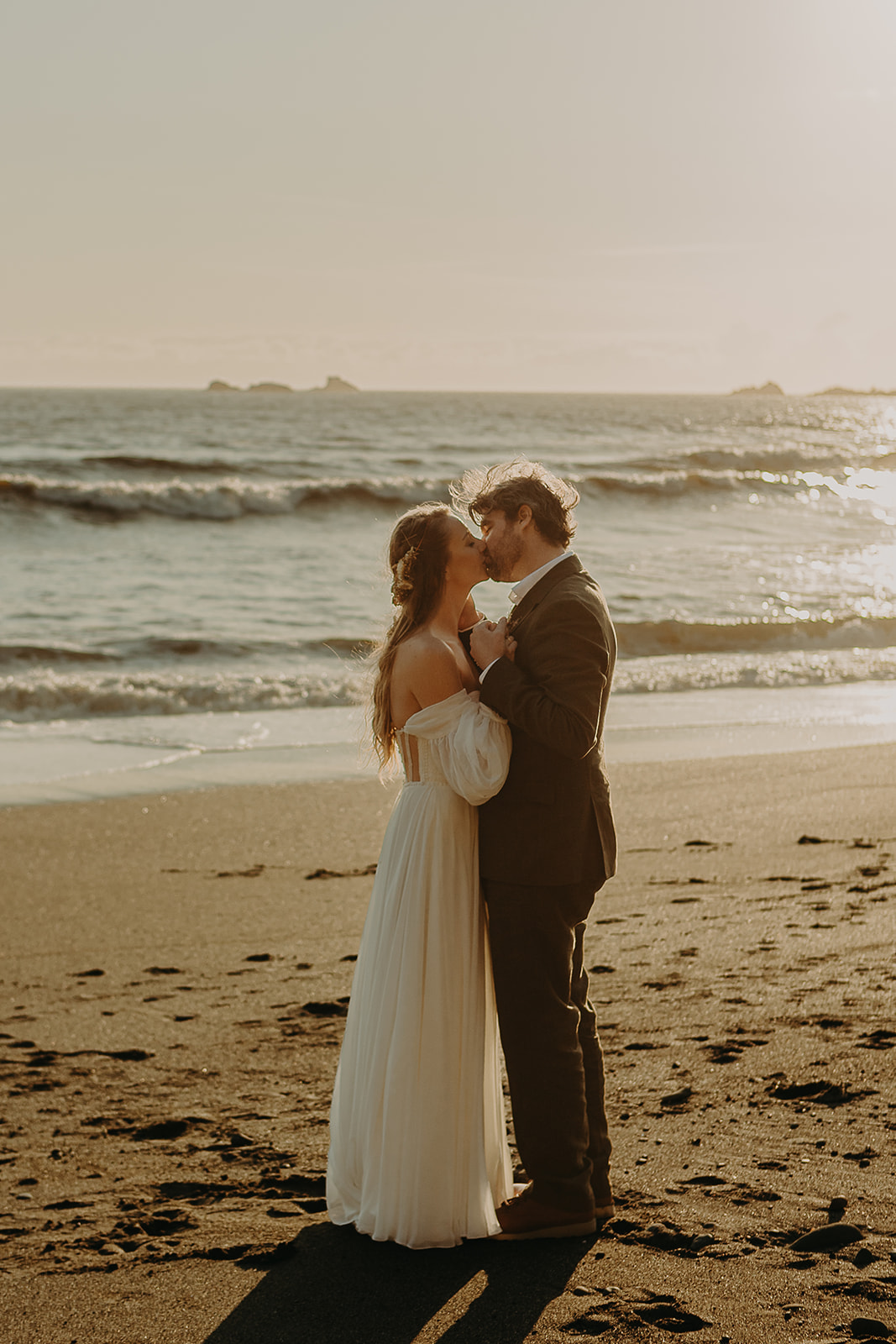 a bride and groom walk kiss on a sandy beach with ocean waves in the background for this Brookings, Oregon elopement.
