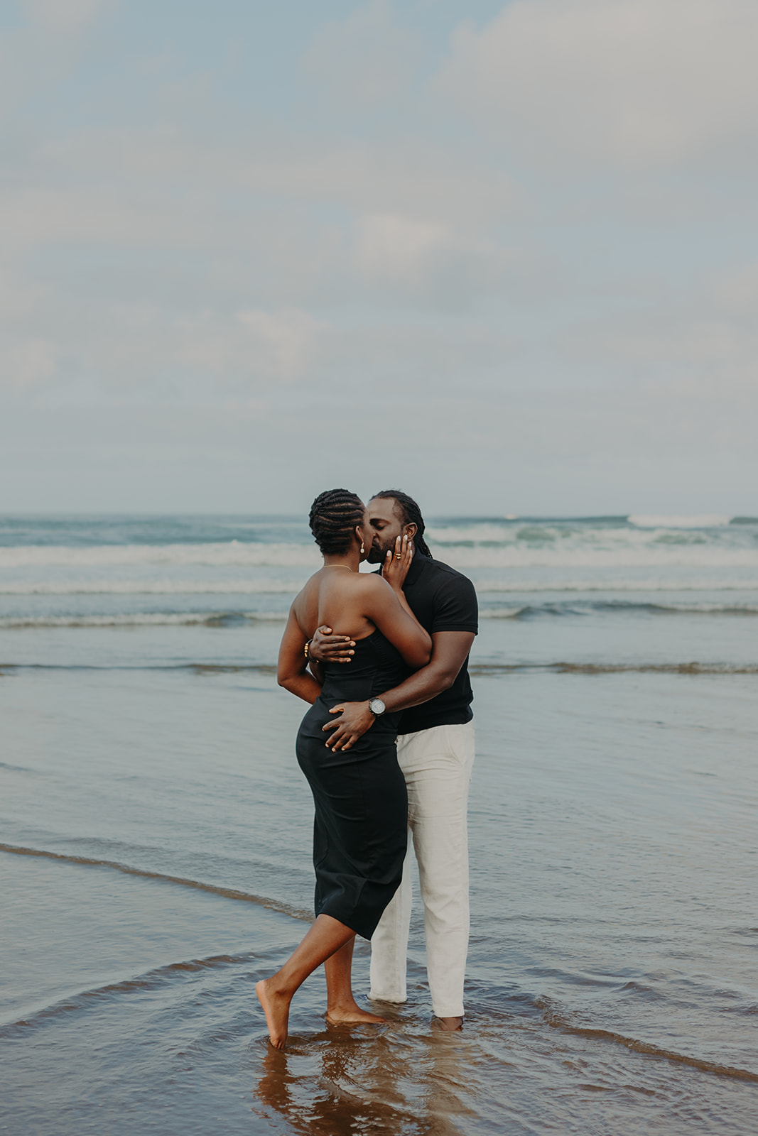 a couple standing on the beach at Haystack Rock in Cannon Beach as waves ripple around them 