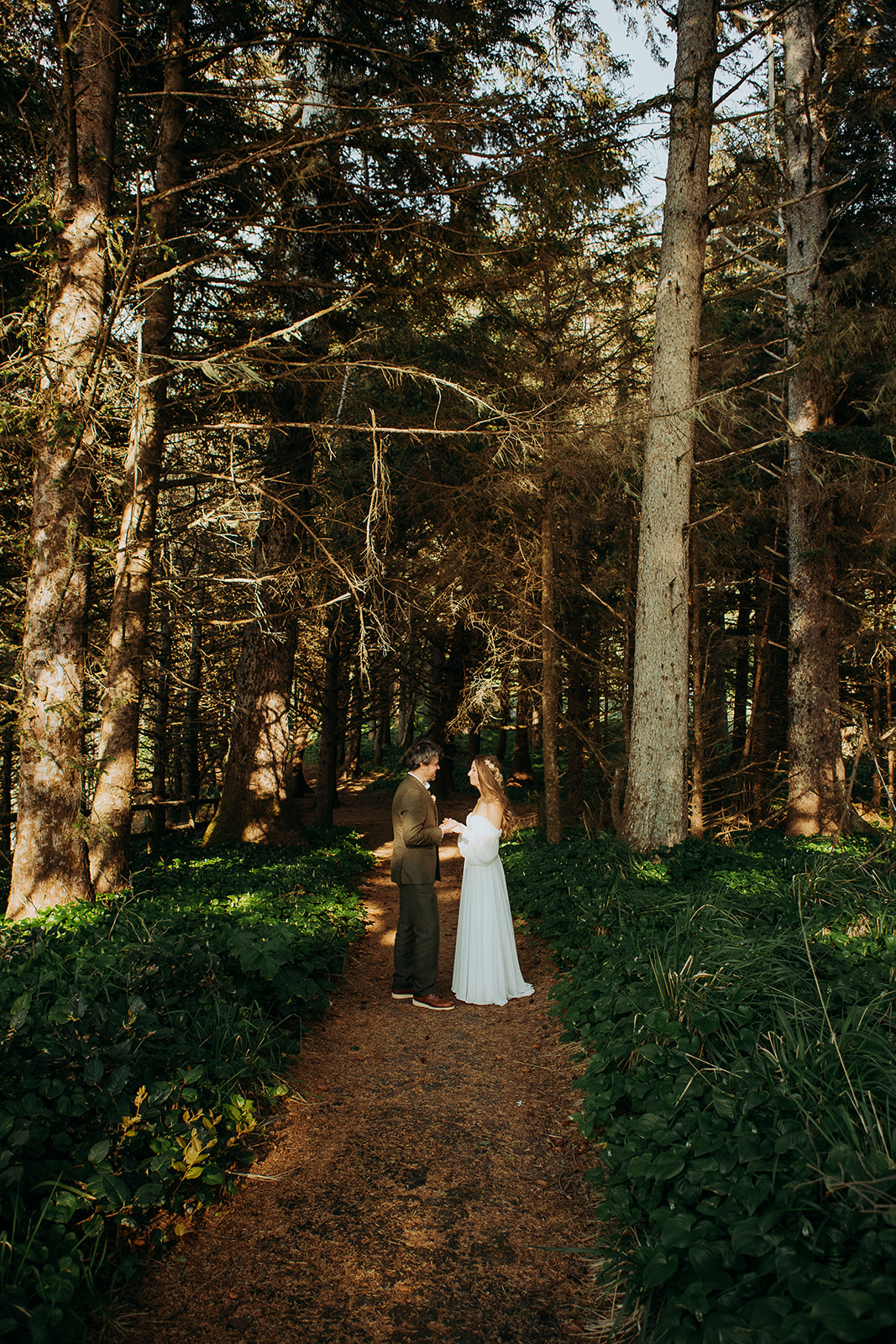 A couple stand hand in hand in a forest dressed in wedding attire. 