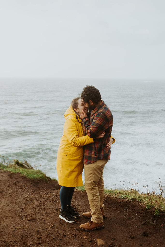 a couple leans in to each other as they stand on the cliff at the Elk Flats trail overlooking the ocean 