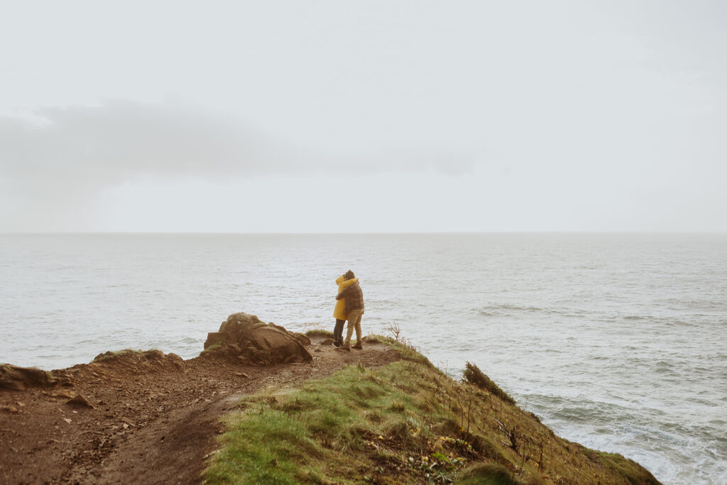 a couple stand on the cliff at the Elk Flats trail overlooking the ocean