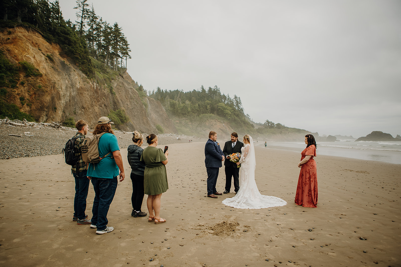a small group of people gather around a couple on a beach as they exchange vows on the Oregon Coast 