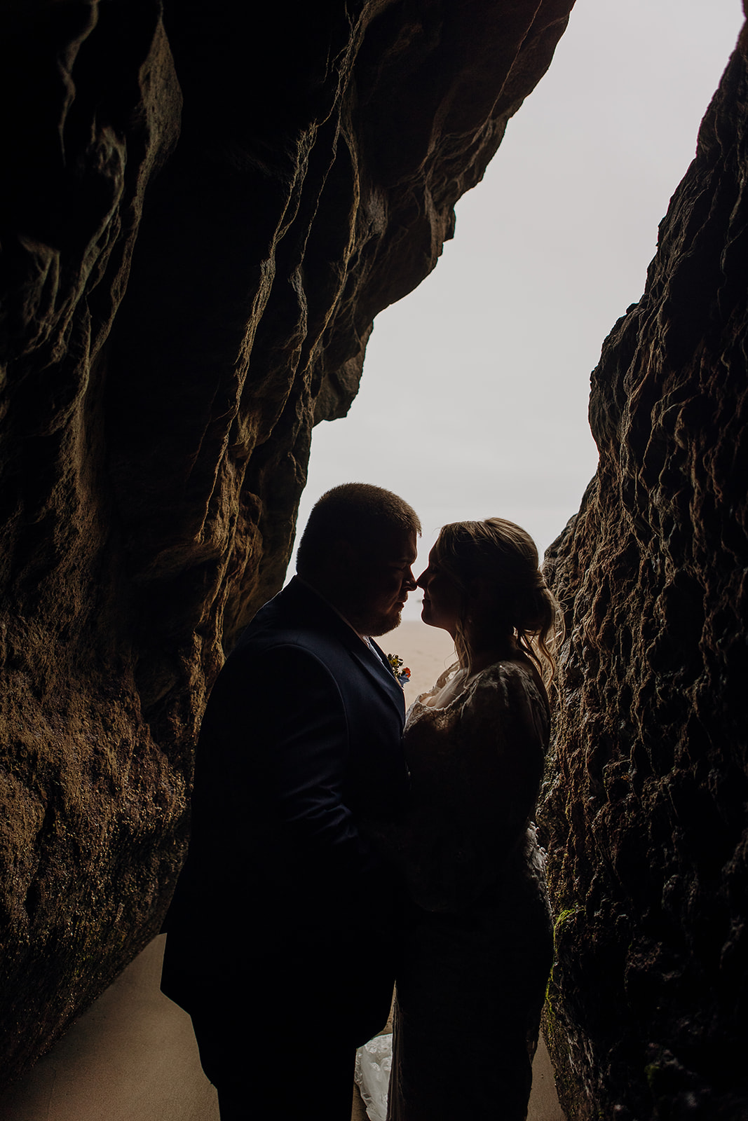 bride and groom stand in front of a cave opening Hug Point State Recreation Site at the Oregon Coast