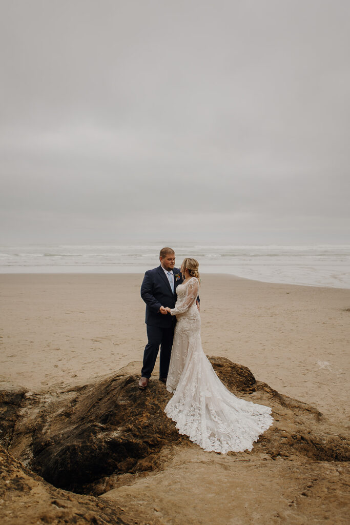 bride and groom stand on a rock outcropping on Hug Point beach with the ocean in the background