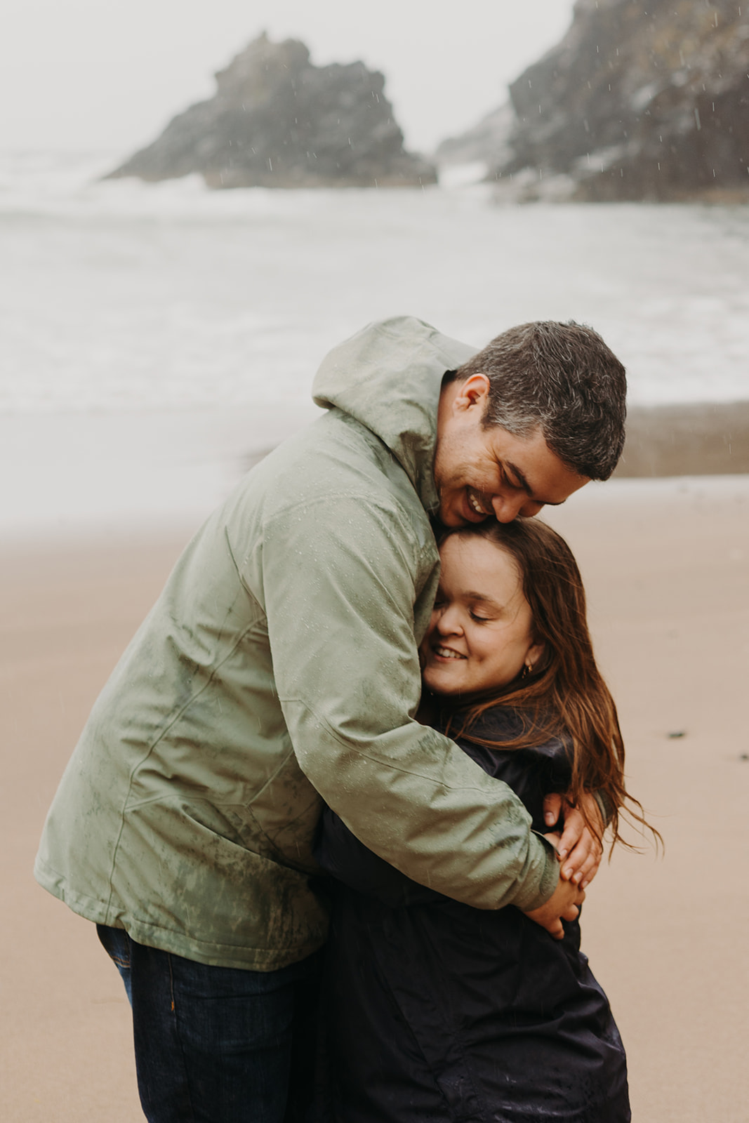 man and woman embrace on the sandy shores of Indian Beach as waves crash in the background