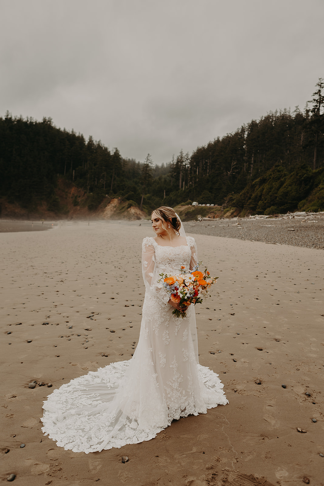 bride stands in her wedding gown on the sandy shores of Indian Beach at Ecola State Park