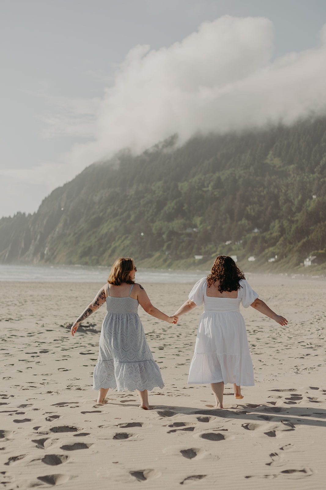 two women run hand in hand on sandy Manzanita Beach 