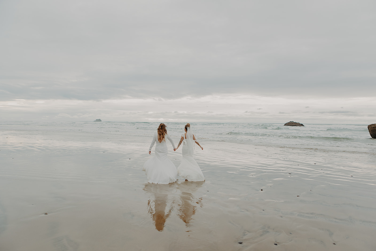 two brides run into the waves on the beach shore of Manzanita in Oregon
