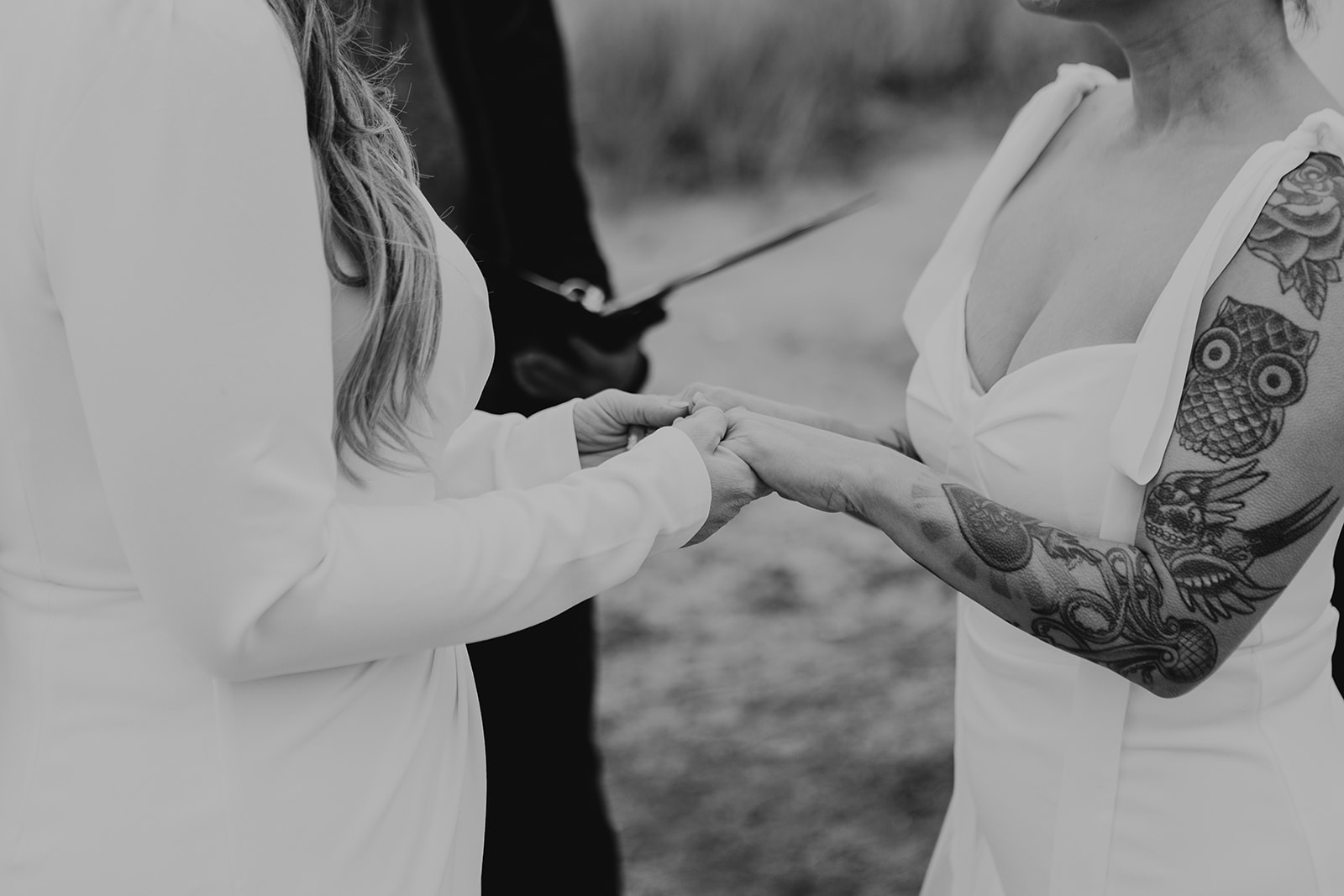 a close up black and white image of two brides holding hands on their wedding day as they exchange vows 