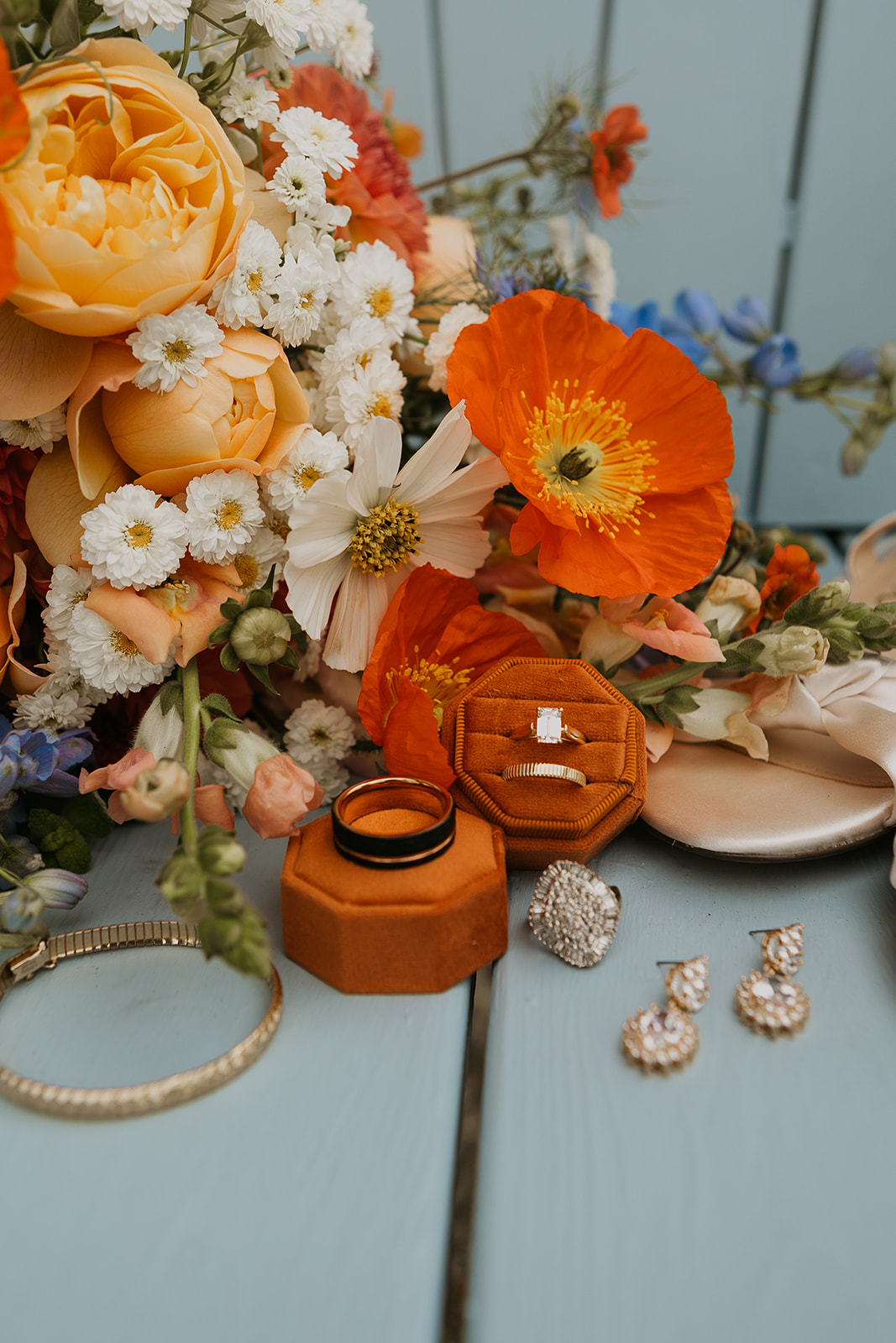 blue and orange wedding bouquet with wedding rings on orange ring box and blue chair