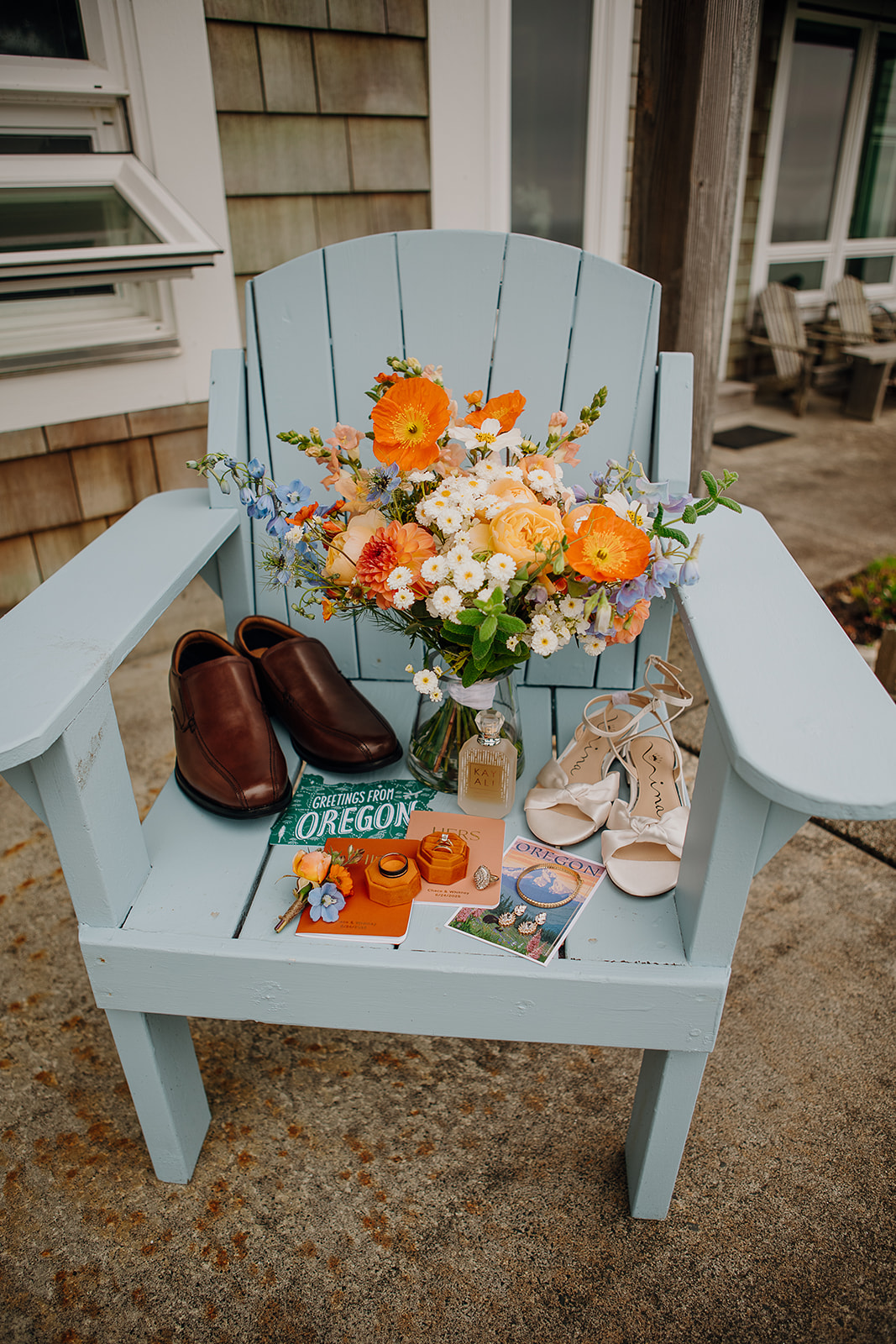 wedding flat lay details such as bouquet, wedding shoes, invitations, and rings sit on a blue chair on the Oregon Coast