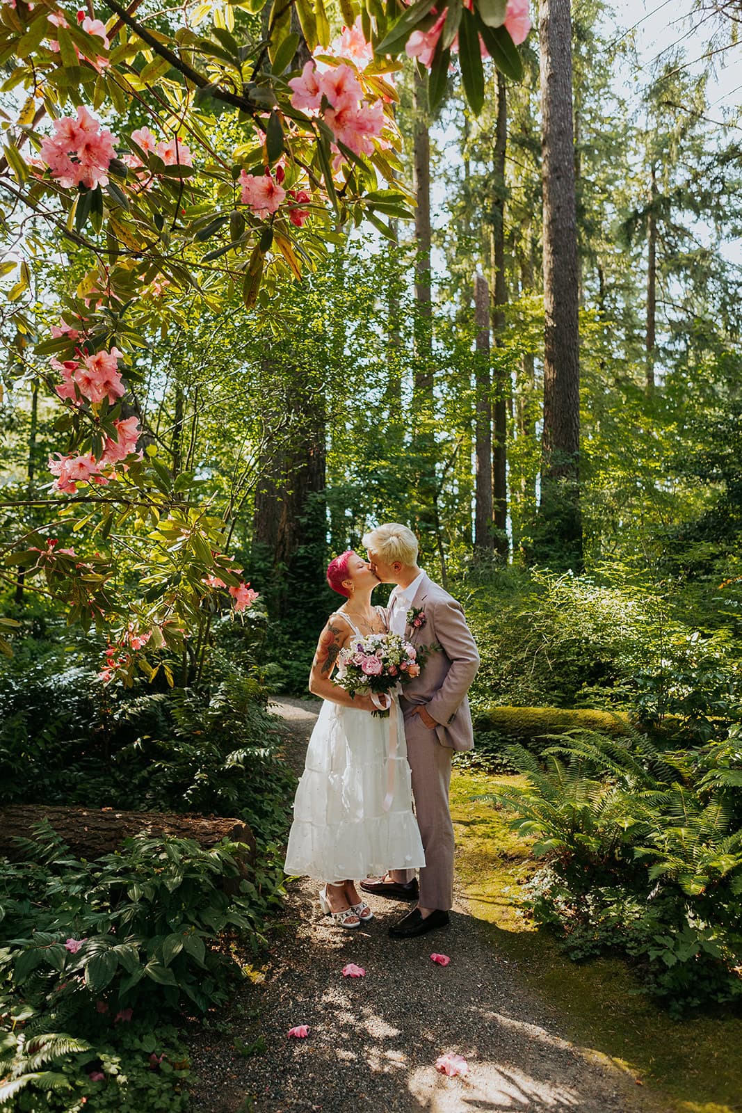 non-binary person with pink hair leans into their groom at Leach Botanical Garden with pink flowers overhead