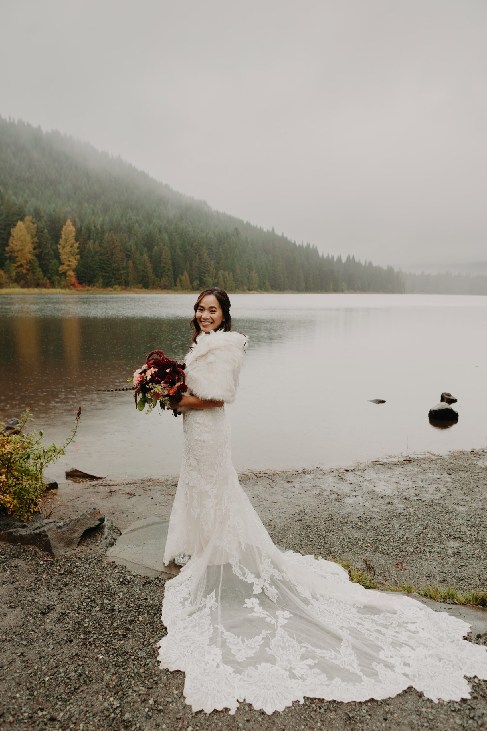 portrait of a bride in a lace wedding dress and fur stole at the shores of Trillium lake at Mount Hood on a misty day