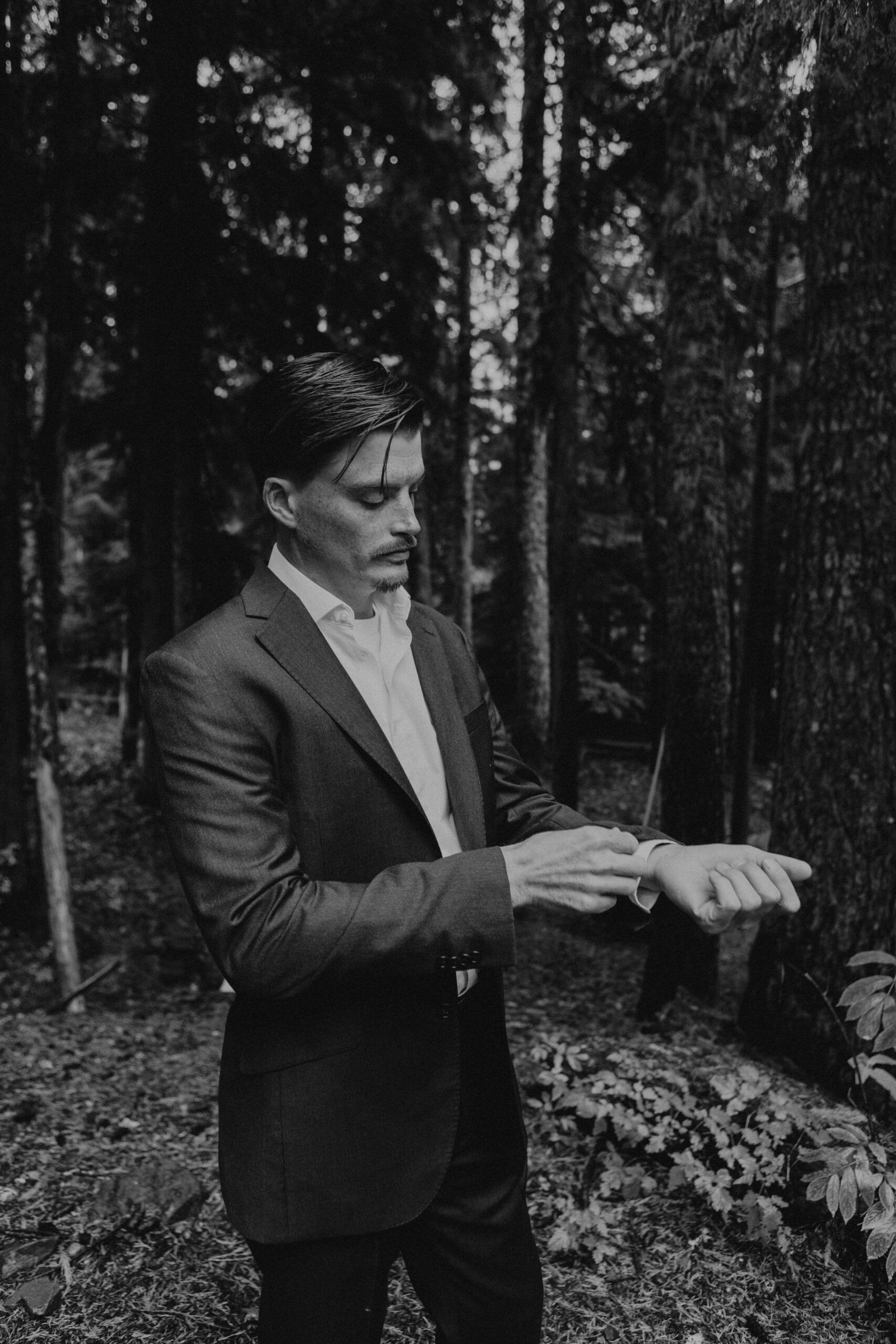 black and white photo of a groom adjusting his cuffs at Mount Hood National forest 