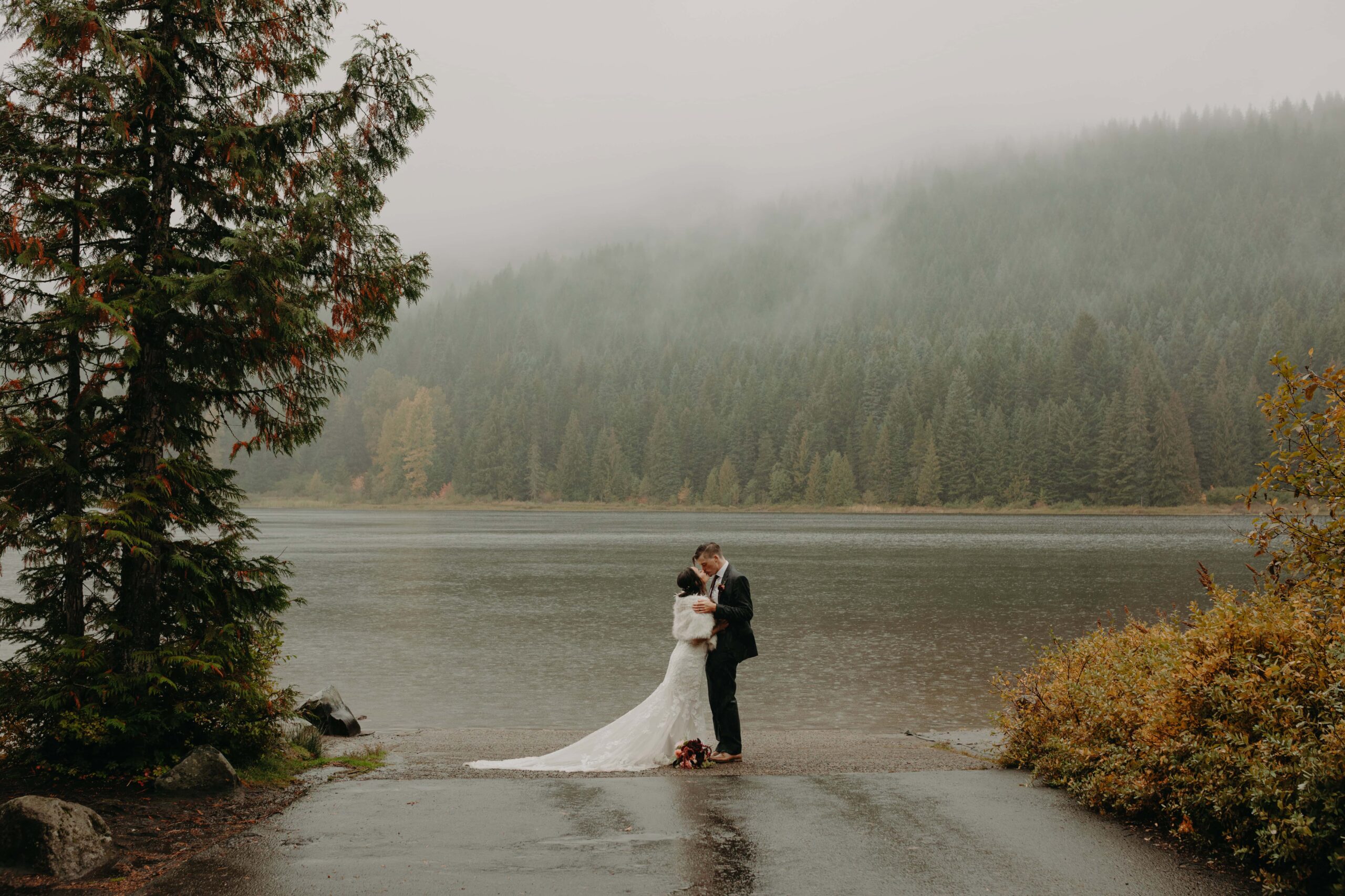 bride and groom kiss at the shore of trillium lake at mount hood as it rains