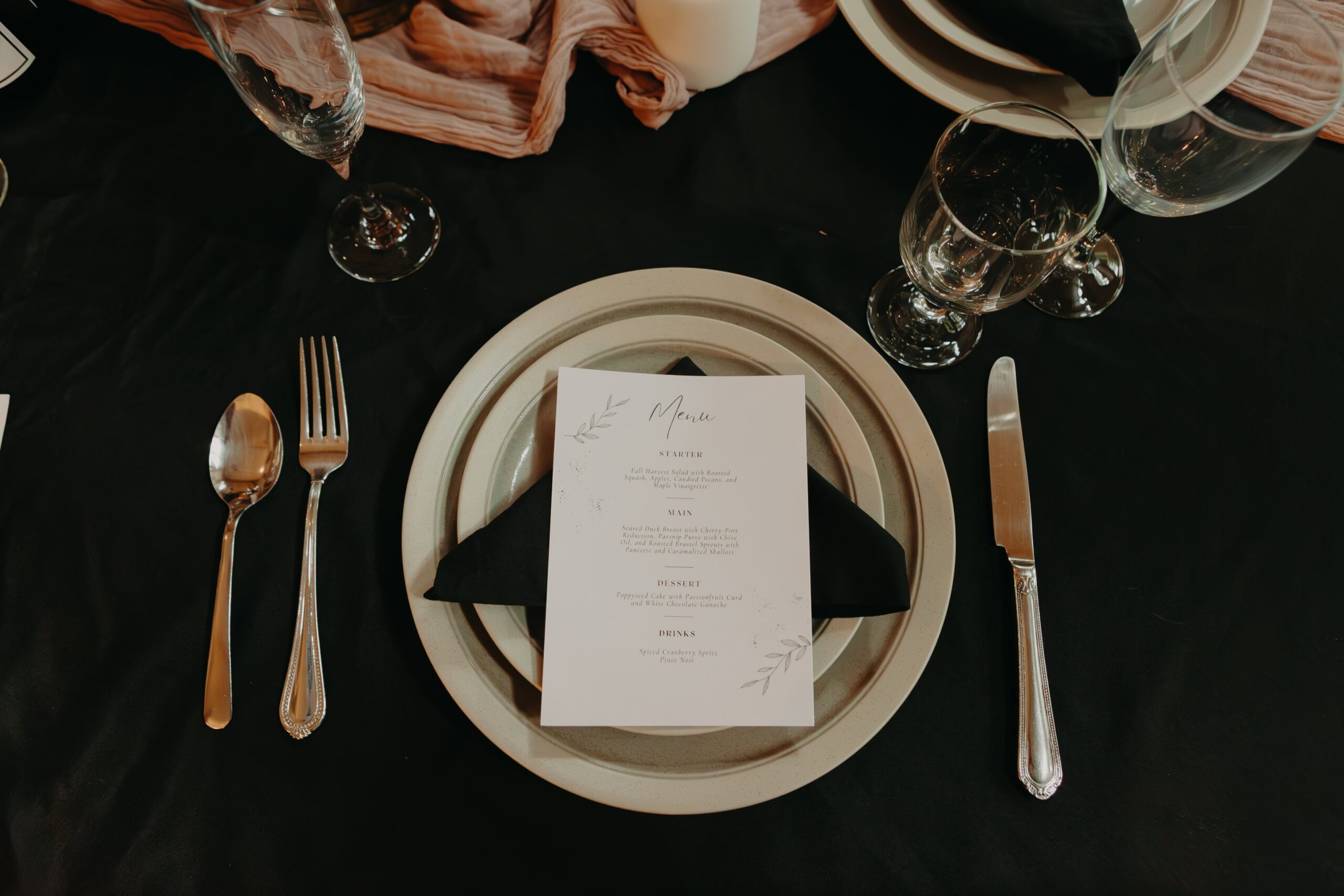 tablescape flatlay of plate with menu on top, silverware, glasses on a black tablecloth