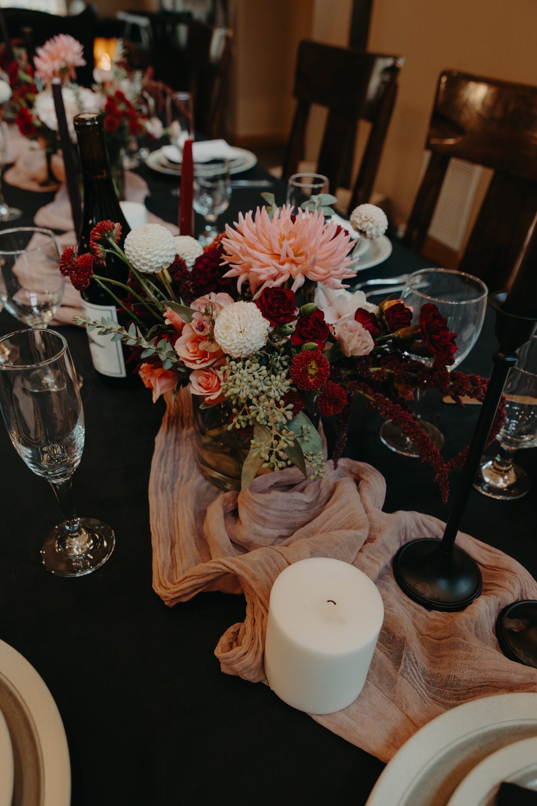 a pink table runner on a black tablecloth with a bouquet of pink and burgundy flowers in the center for this wedding tablescape
