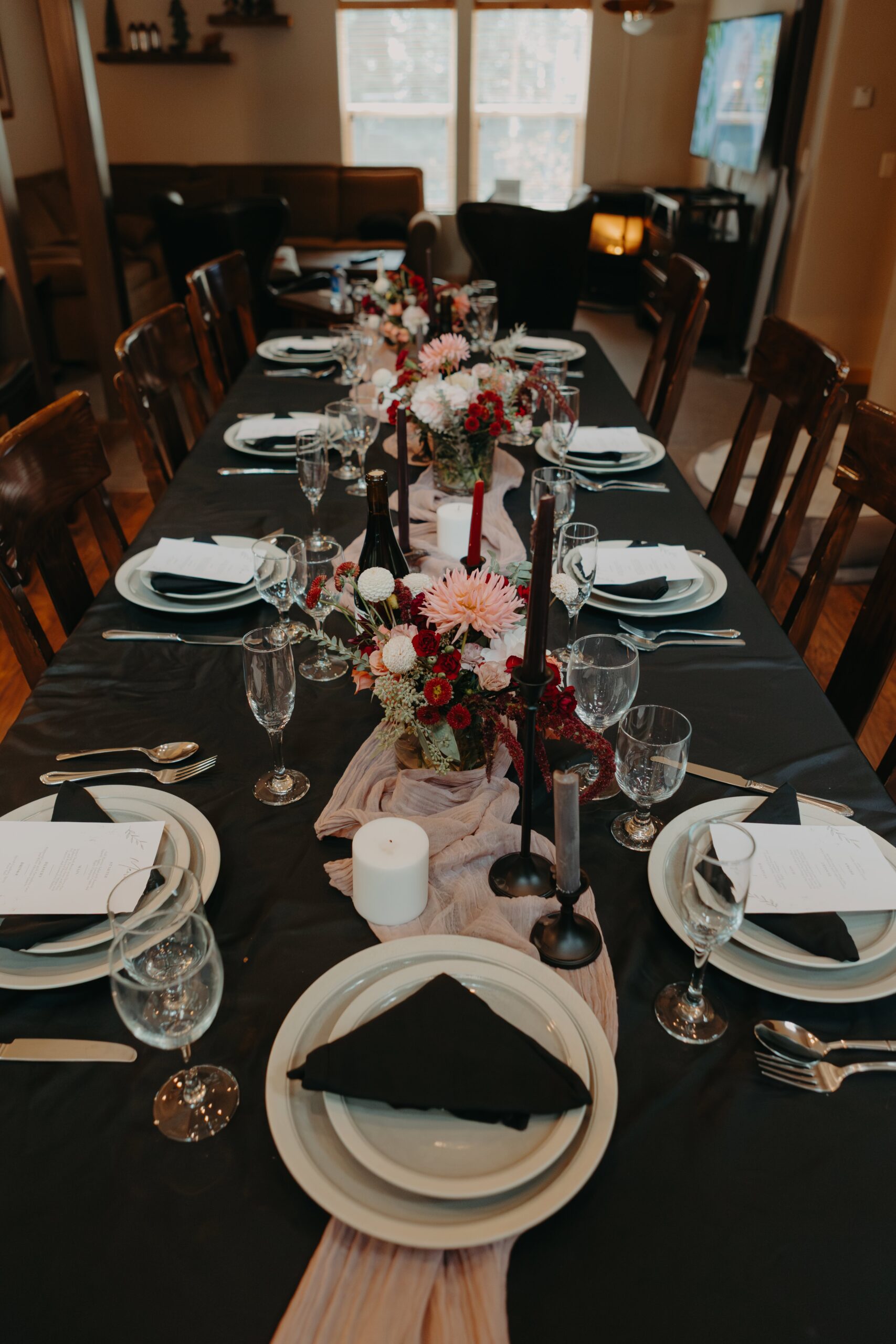 a pink table runner on a black tablecloth with a bouquet of pink and burgundy flowers in the center for this wedding tablescape with dishes and plates
